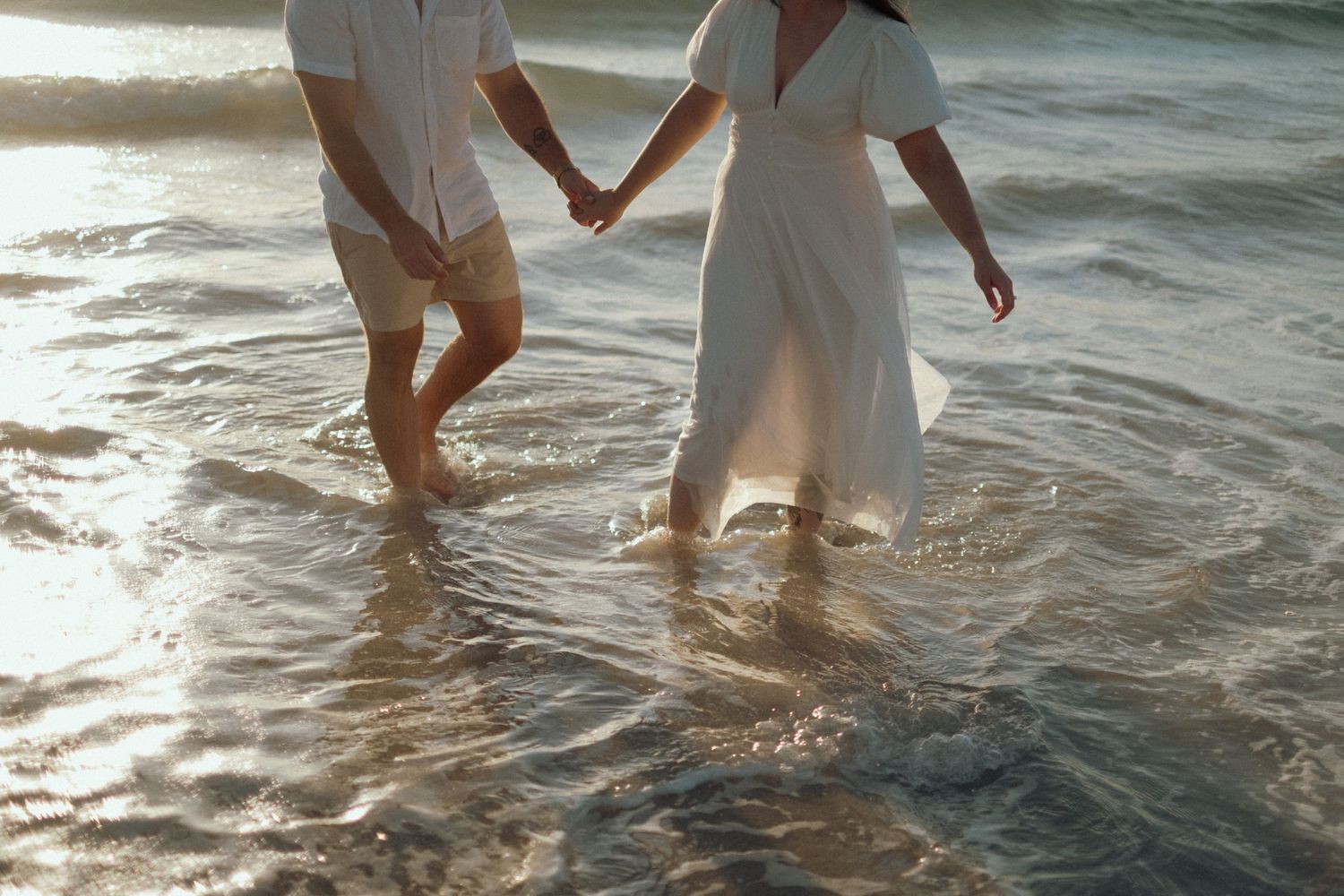 Legs and feet wading in gentle ocean waves during a beach photoshoot.