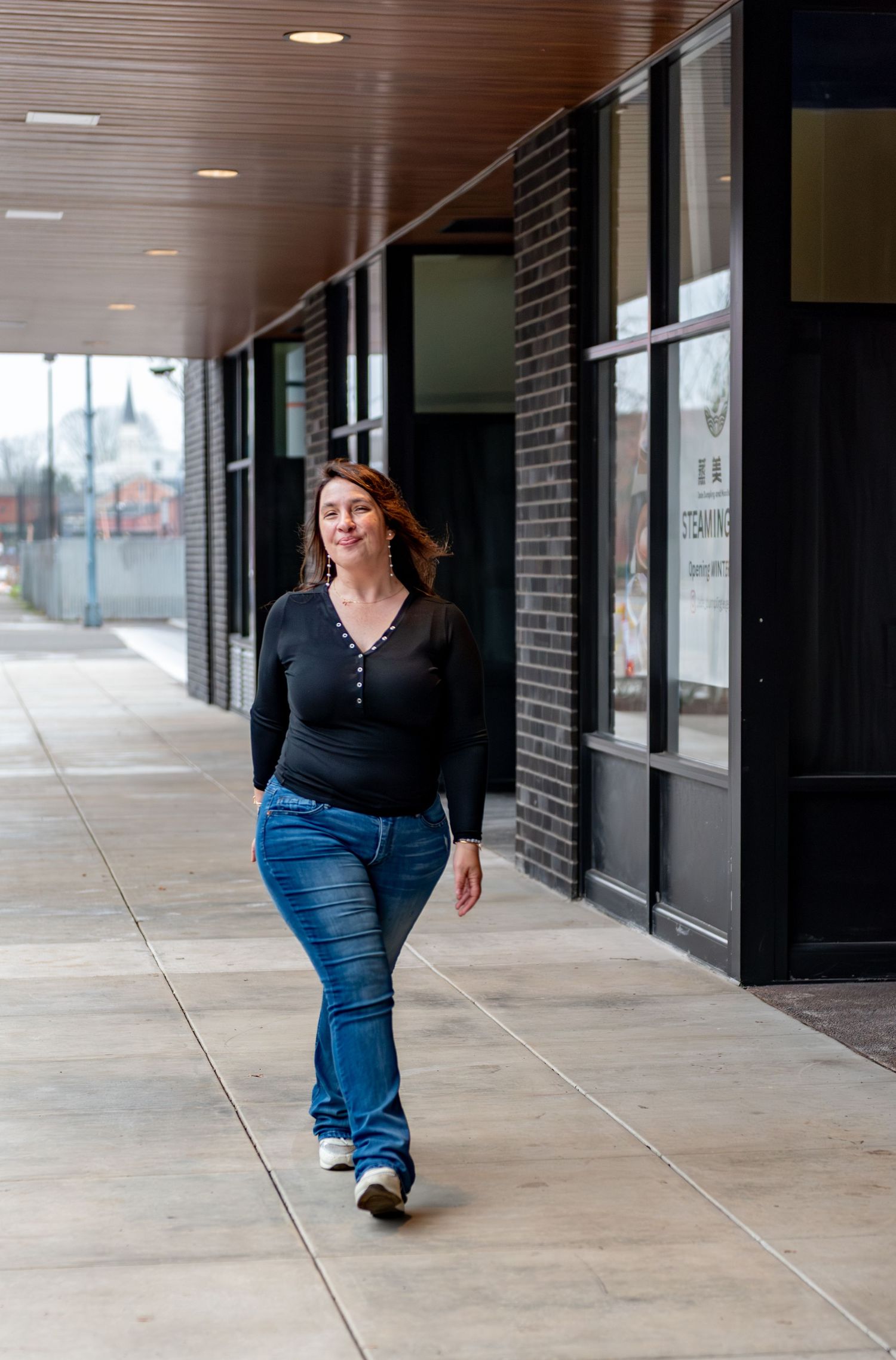 Woman walking on sidewalk with neutral brick background and industrial black framed windows for a branding session, Downtown Salem, OR