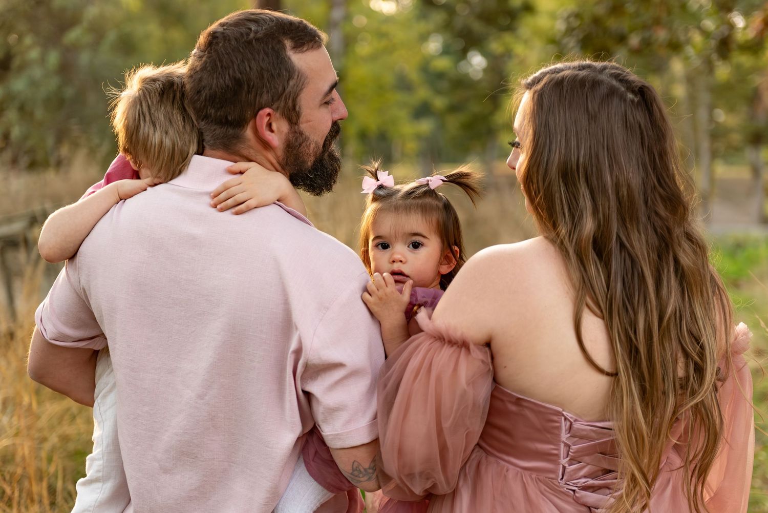 Family of four portrait located in a field with fall colored trees in the background and natural golden hour light. Located in Salem, OR