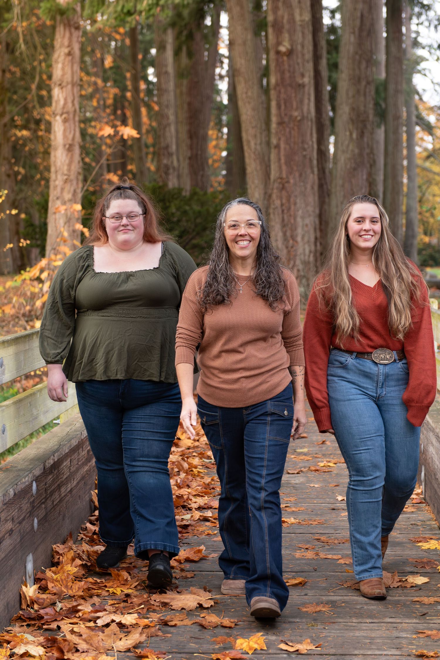 A group of people stand together on a wooden bridge surrounded by tall trees in autumn. located in Stayton, OR