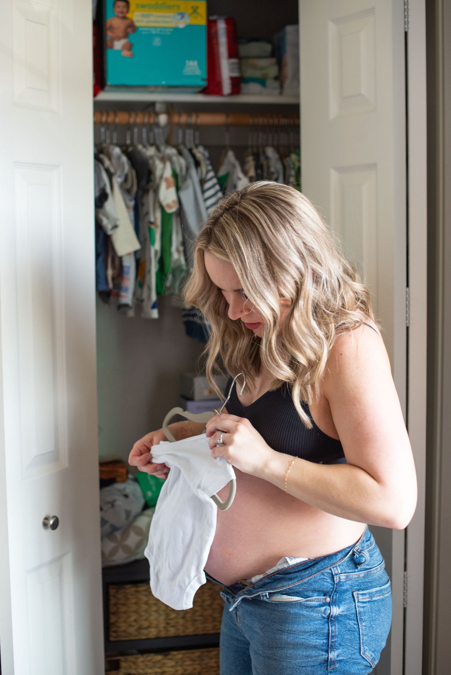 A pregnant woman in jeans and black top looks through baby clothes in a closet. Located in Salem, OR