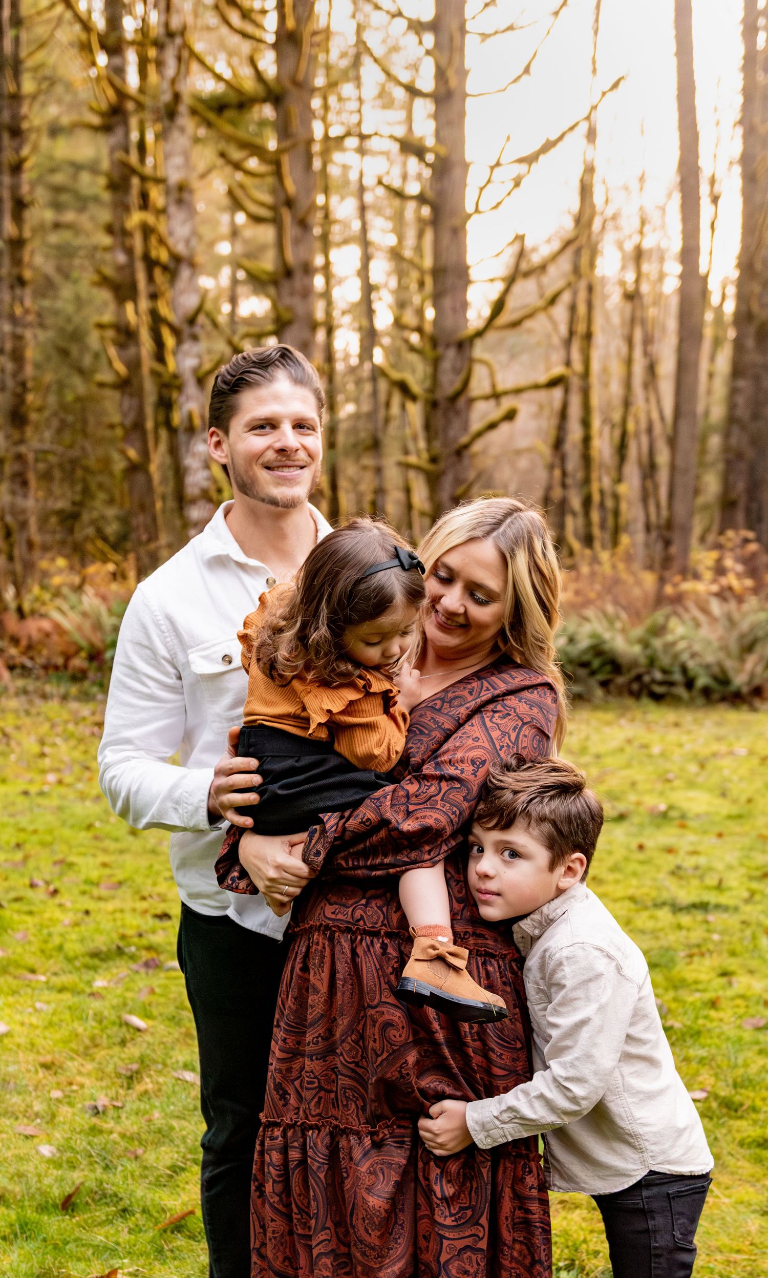 A family shares a joyful moment together in an autumn forest clearing with tall trees in the background. Silver Falls State Park, OR