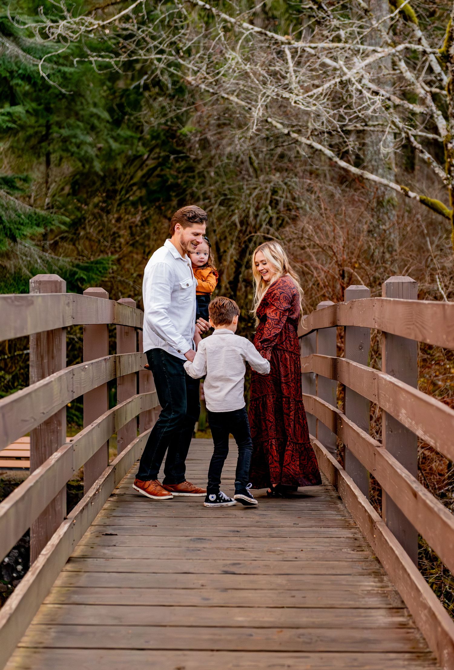 A family shares joyful moments together while posing for photos on a wooden bridge in an autumn setting. Silver Falls State Park OR