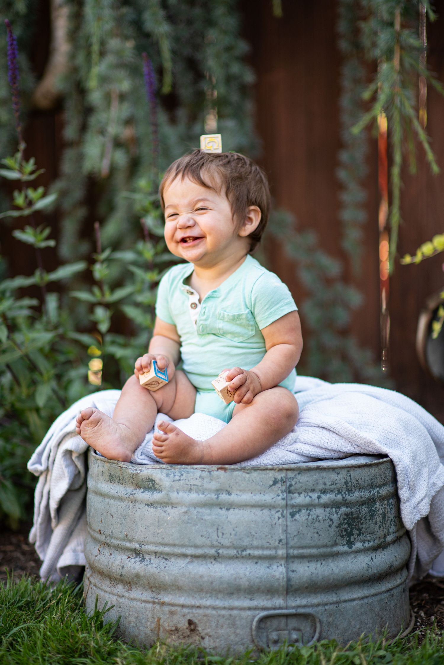 Toddler sitting on an upside down metal basin with a block balanced on his head, Springtime flowers, Salem, OR.
