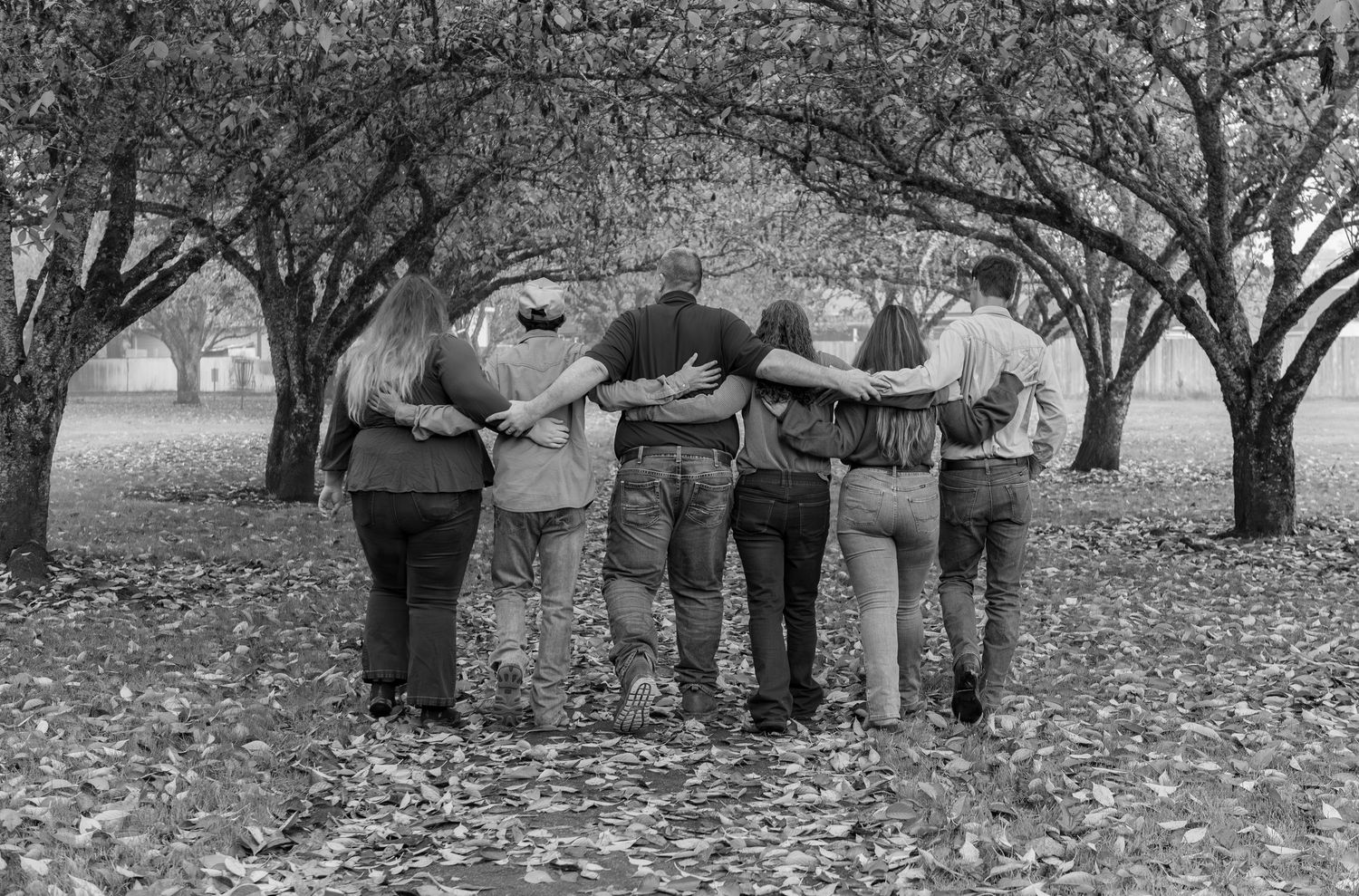 black and white photog showing people walking through a park with fallen autumn leaves on the ground. Stayton, OR