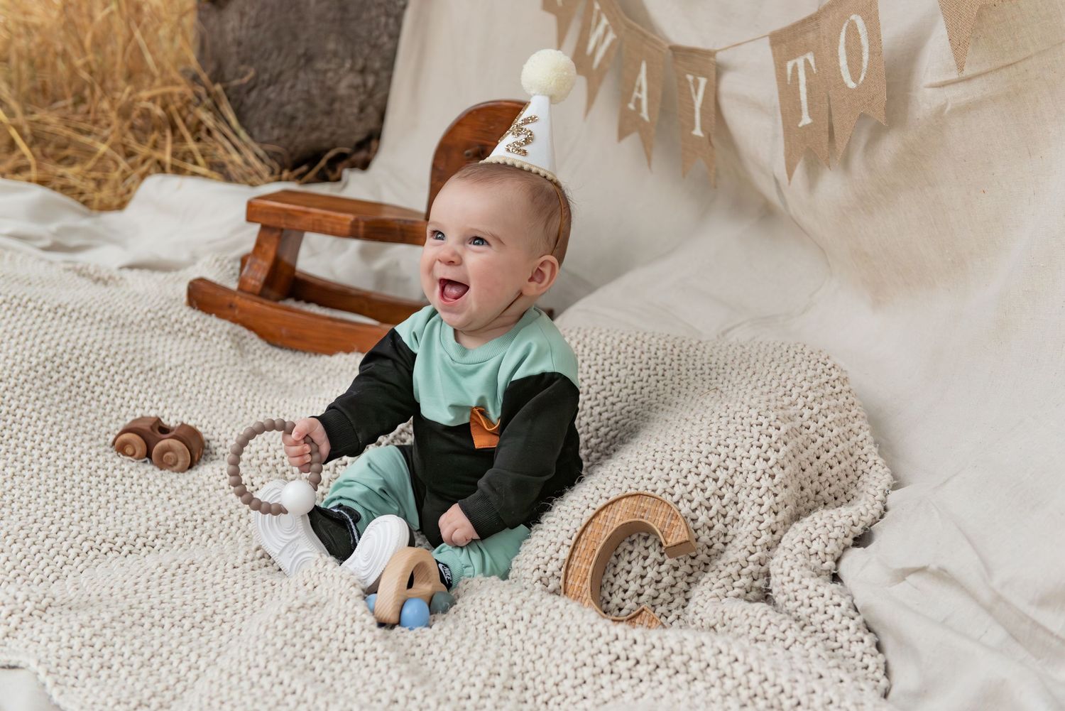 Six month milestone image with baby laying on a blanket, smiling and interacting with parents. Neutral backdrop with lettering. Salem, OR.