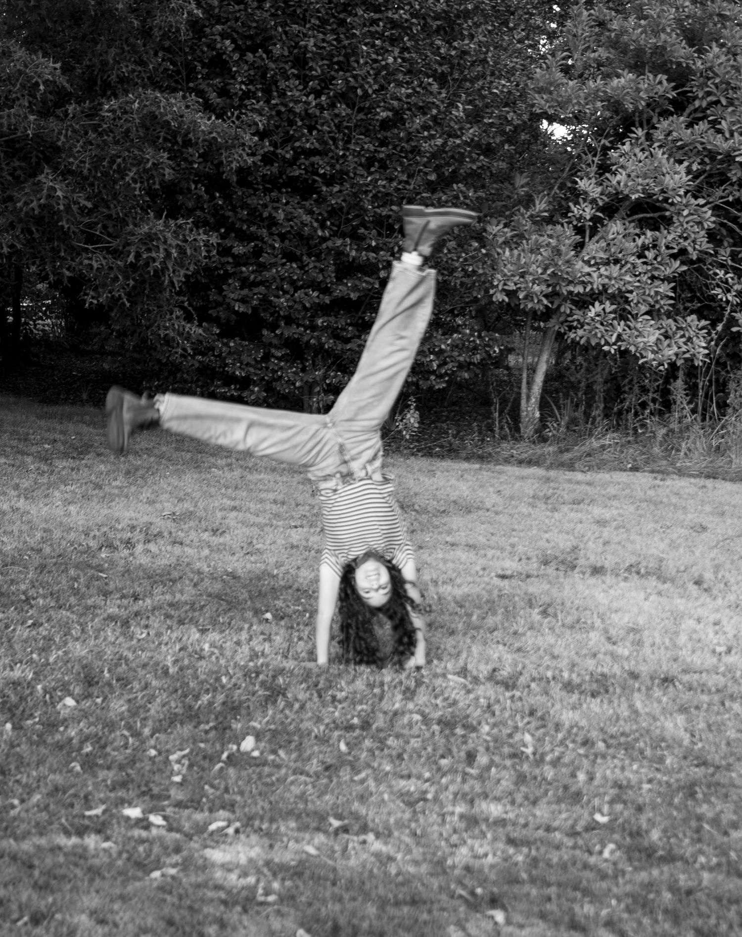 Young girl mid cartwheel in a black and white photo, grassy area with trees in the background. Salem, OR.