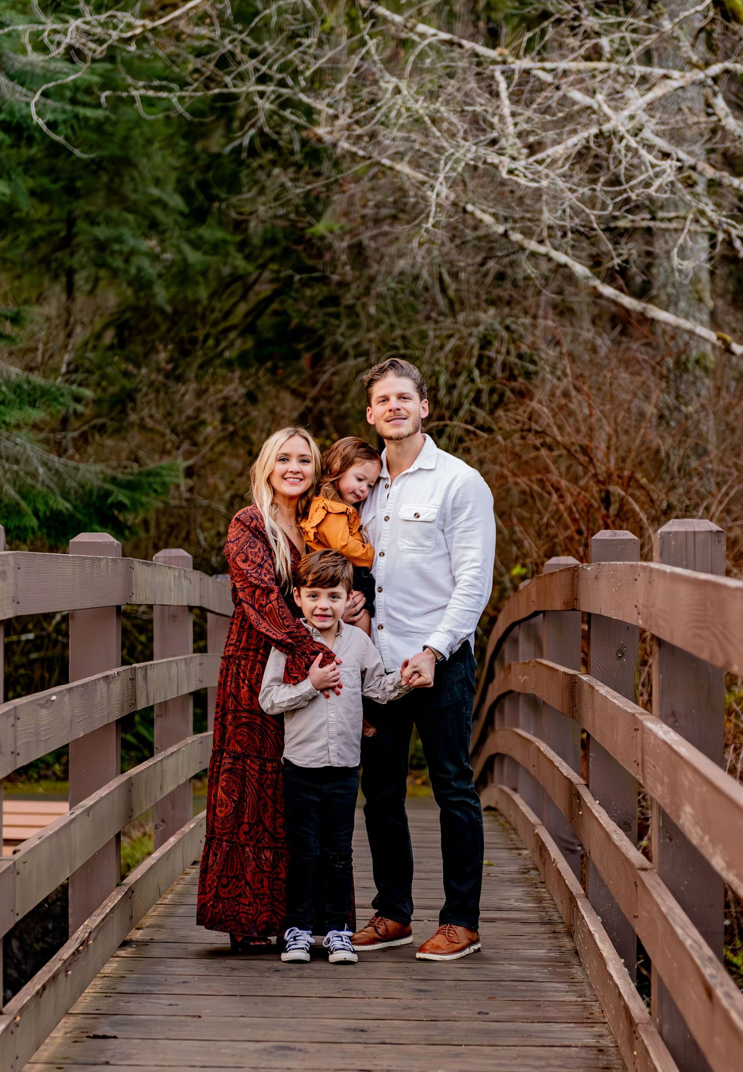 A family shares joyful moments together while posing for photos on a wooden bridge in an autumn setting. Silver Falls State Park OR