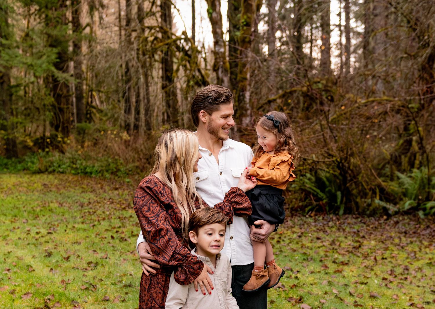 A family in coordinating outfits walks together through a lush green forest setting during a photo session. Silverton, OR