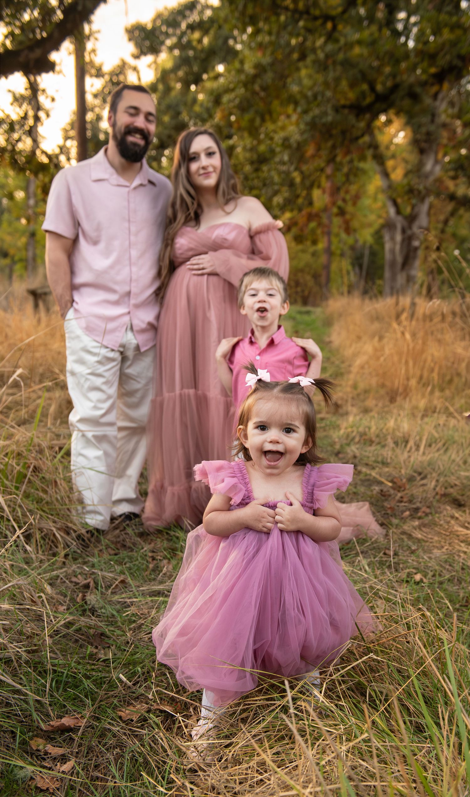Family of four portrait located in a field with fall colored trees in the background and natural golden hour light. Located in Salem, OR