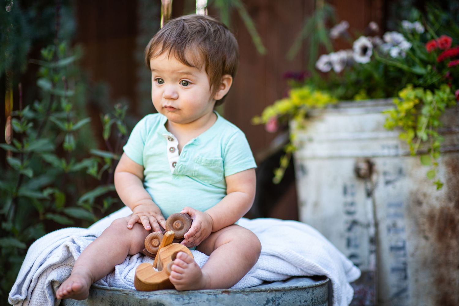 A baby in a mint green outfit sits outdoors on a white blanket while playing with a small toy.