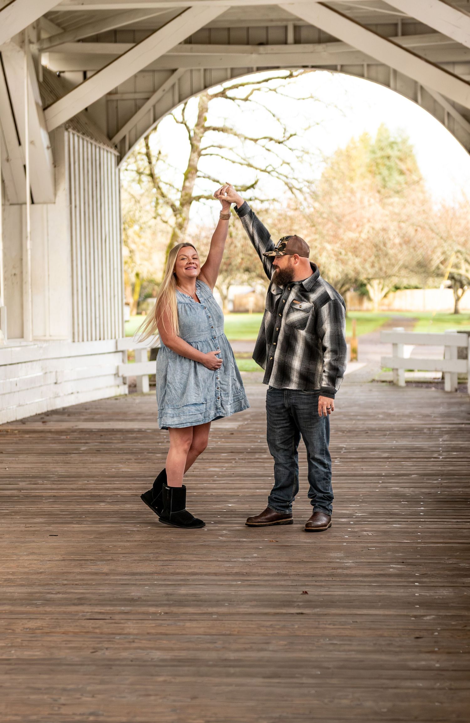 Dad twirling mom under a covered bridge while she embraces her belly in Stayton OR