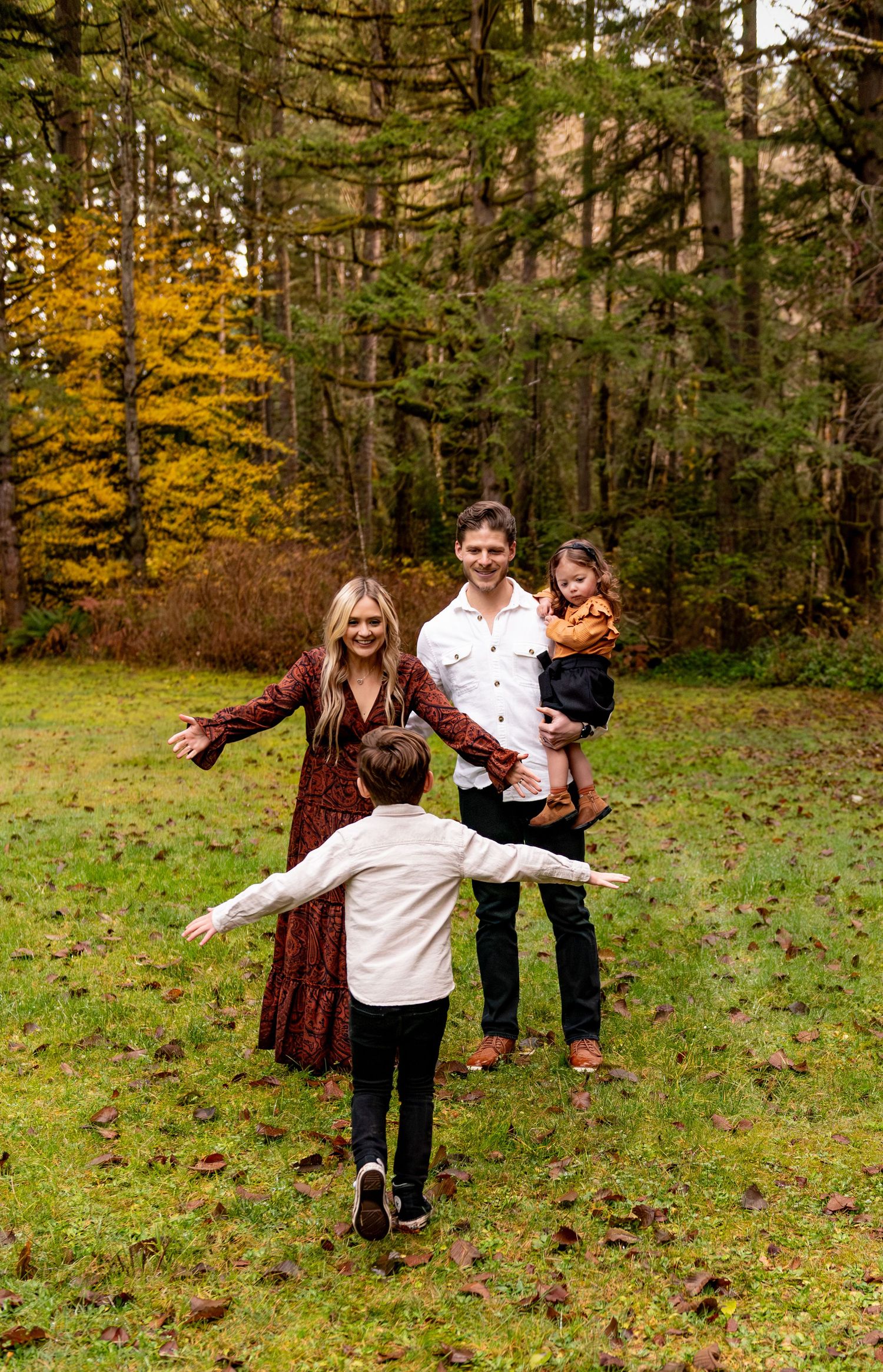 A family plays  together in a grassy field surrounded by autumn trees and fallen leaves. Silverton, OR