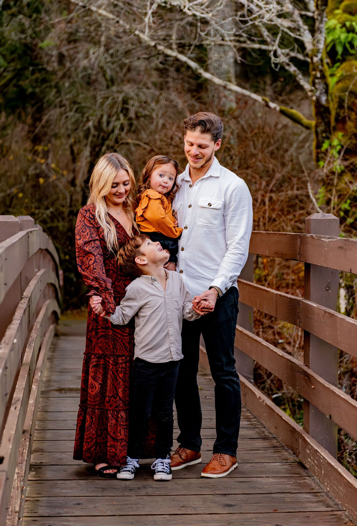 A family shares joyful moments together while posing for photos on a wooden bridge in an autumn setting. Silver Falls State Park OR