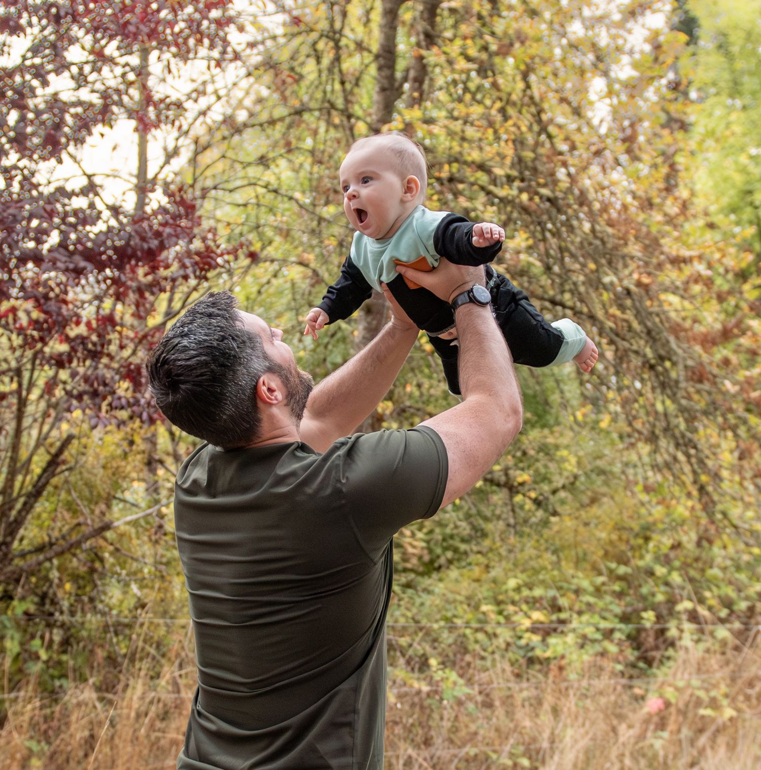 Dad tossing toddler playfully in a wooded area during autumn with warm golden light. Salem, OR