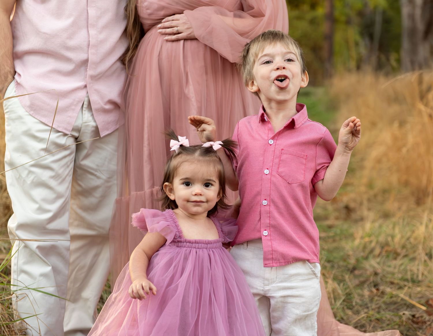 Family of four portrait located in a field with fall colored trees in the background and natural golden hour light. Located in Salem, OR
