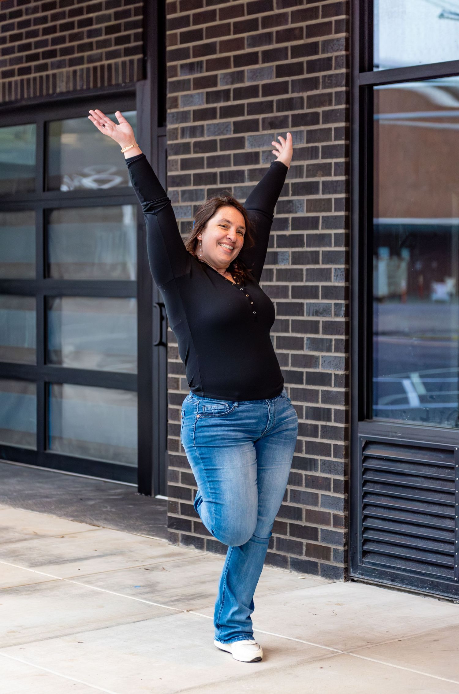 Woman walking on sidewalk with neutral brick background and industrial black framed windows for a branding session, Downtown Salem, OR.