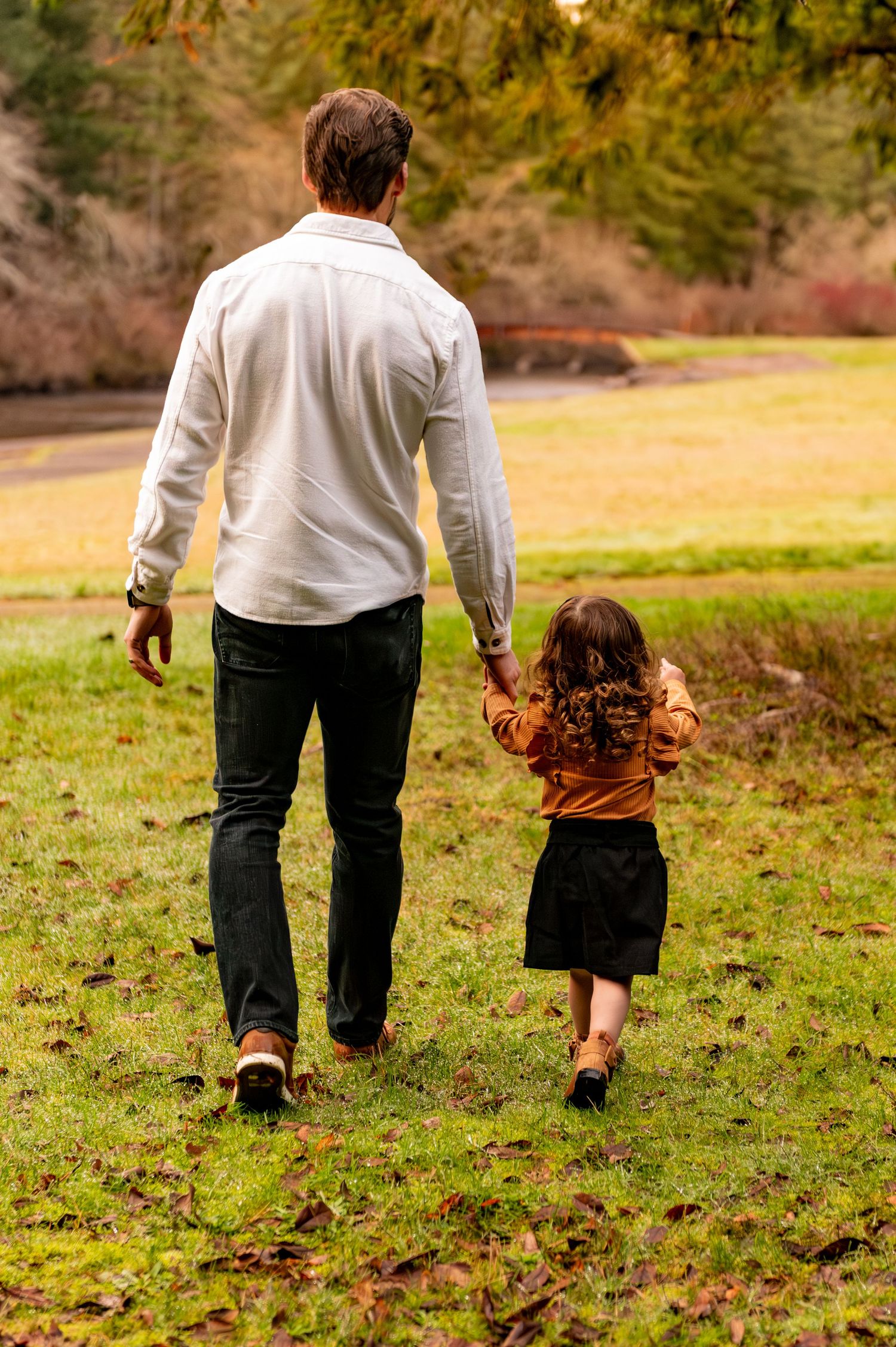 Two people walk together through a grassy autumn field with fallen leaves scattered on the ground. Silverton, OR