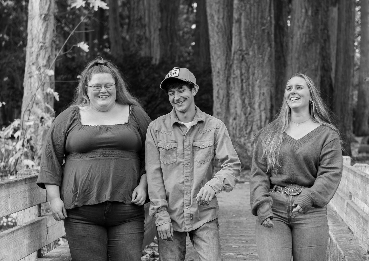 A group of people stand together on a wooden bridge surrounded by tall trees in autumn. located in Stayton, OR