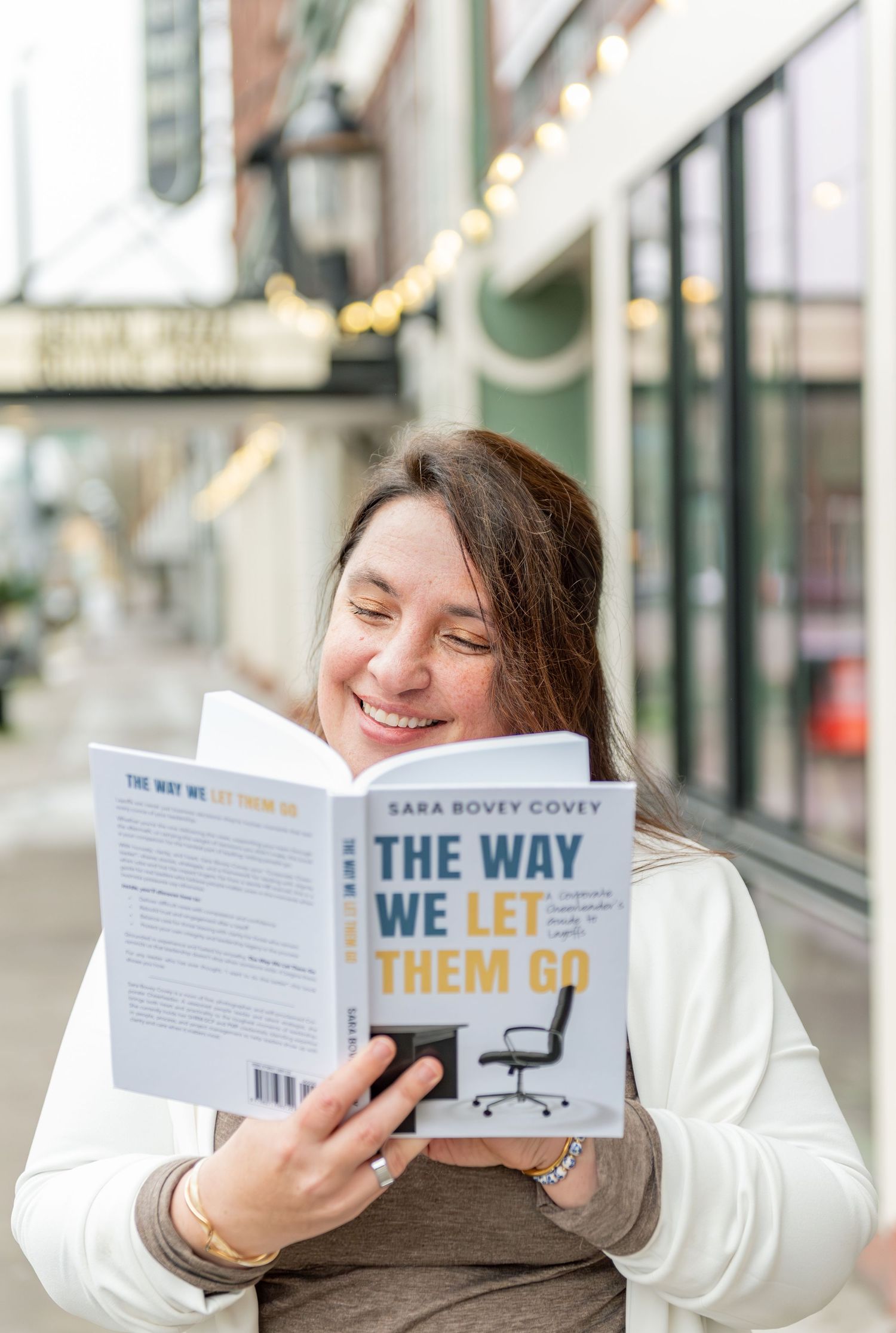 Author reading her book while posed on a sidewalk with a beautiful storefront and string lights in the background. Downtown Salem, OR