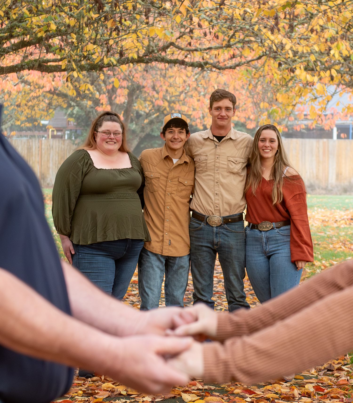 A group stands together in autumn leaves wearing coordinated casual outfits in earth tones during a fall photoshoot. located in Stayton, OR