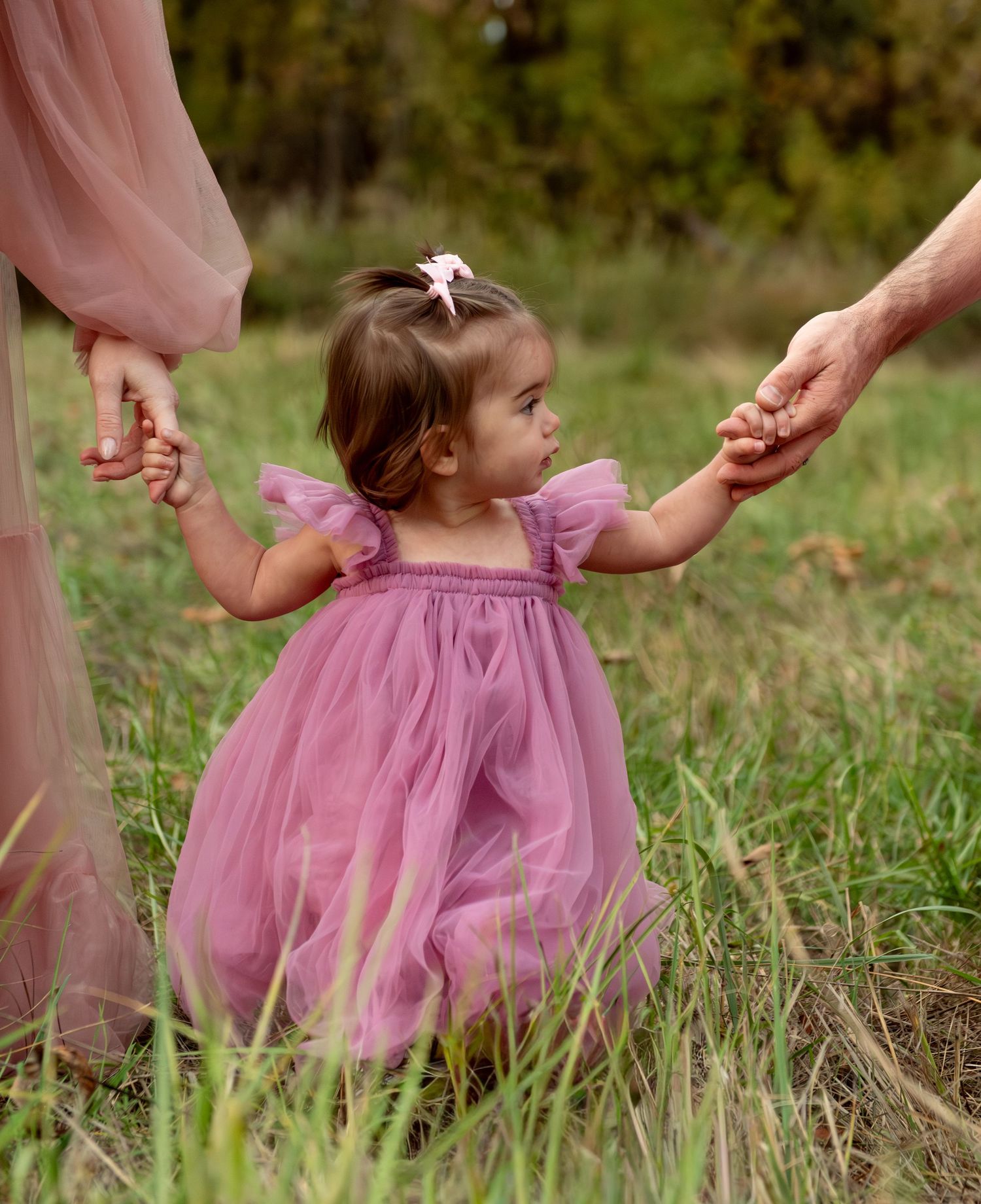 Toddler girl holding mom and dads hand located in an open field in Salem, OR
