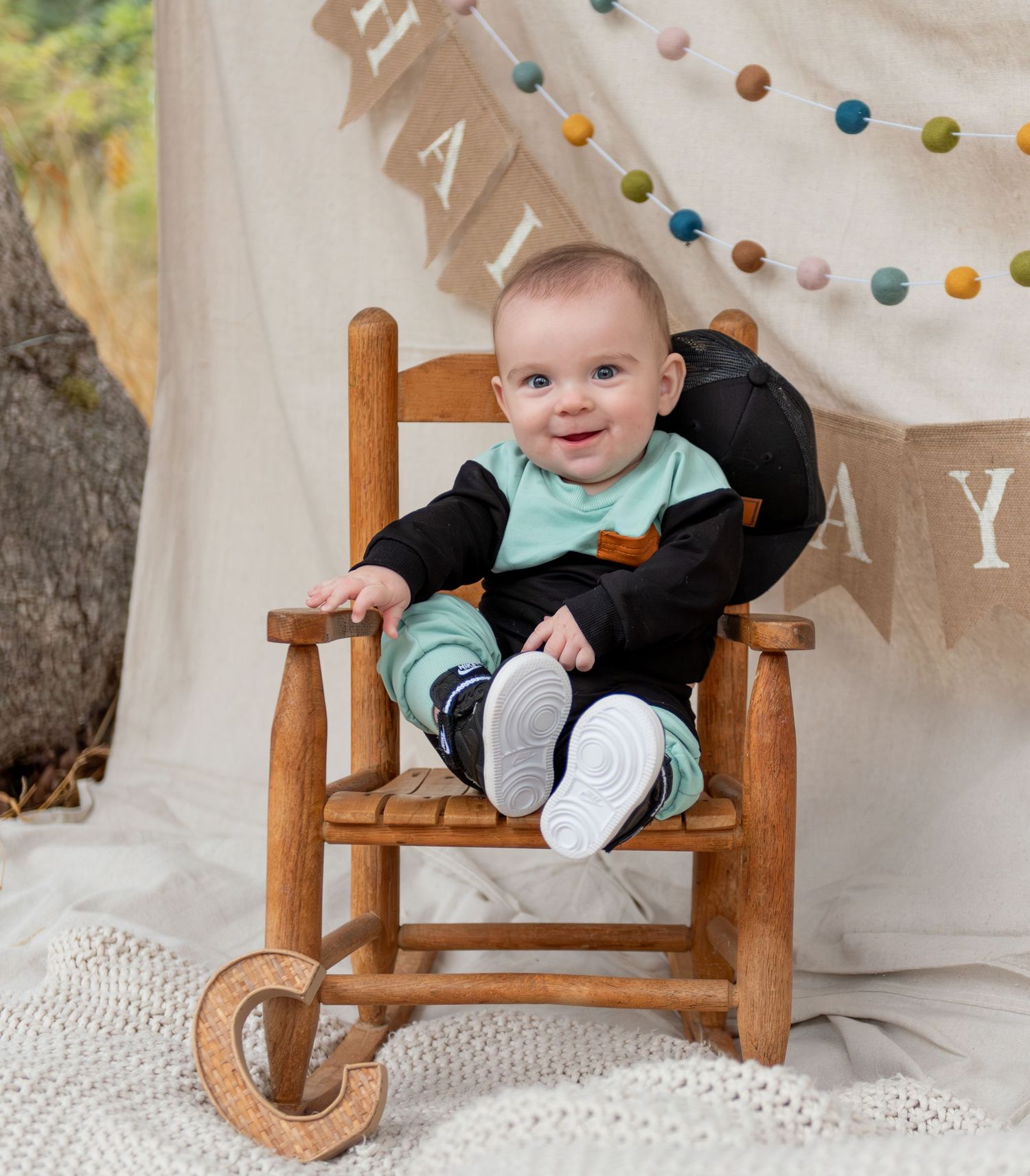 Six month milestone image with baby laying on a blanket, smiling and interacting with parents. Neutral backdrop with lettering. Salem, OR.
