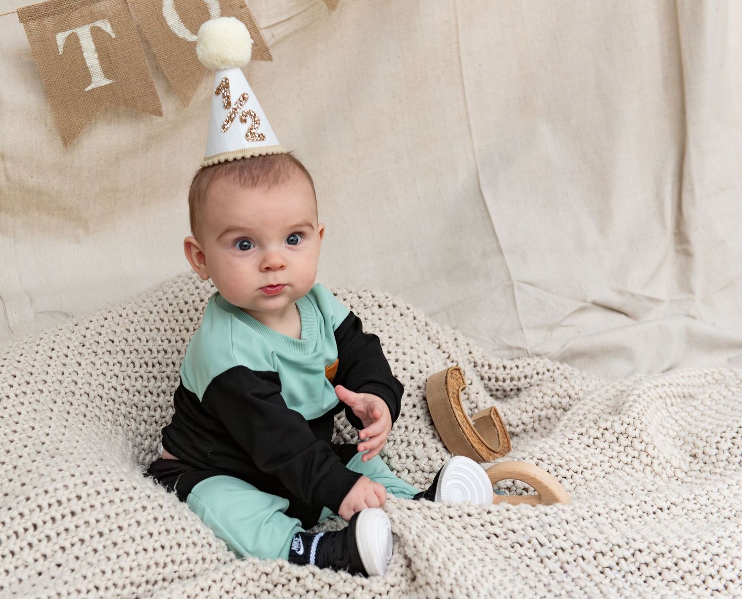 Six month milestone image with baby laying on a blanket, smiling and interacting with parents. Neutral backdrop with lettering. Salem, OR.
