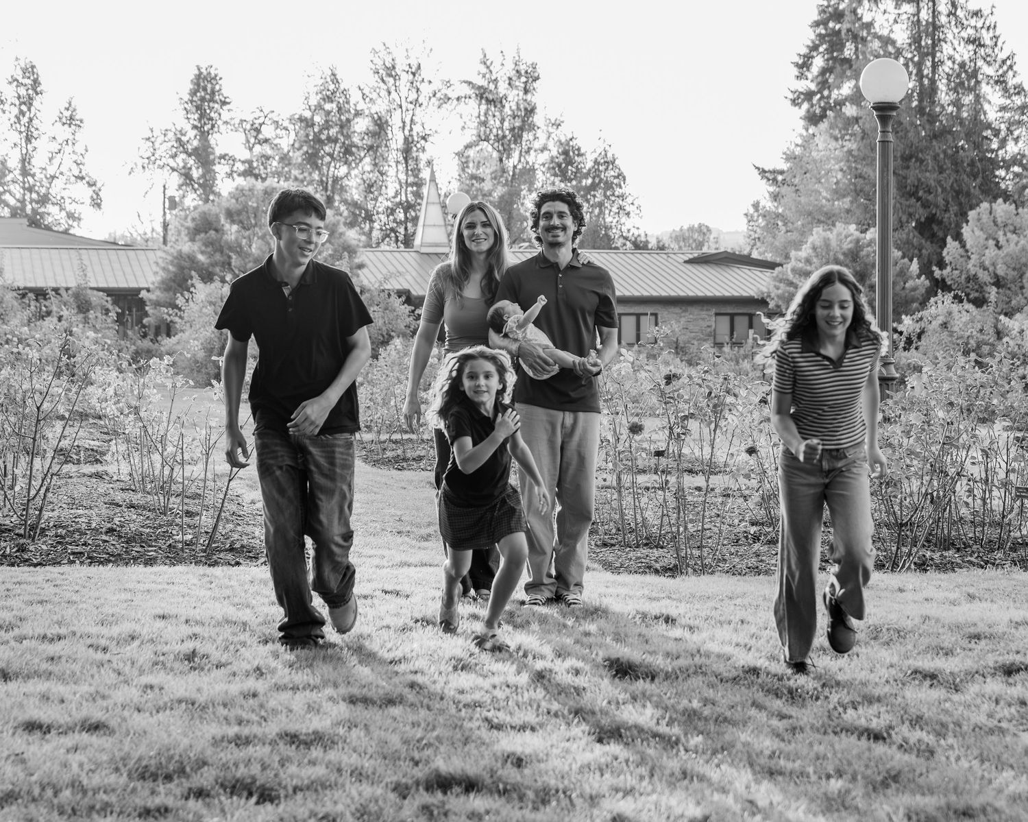 Mom and Dad Posed in the background with children running wildly to the camera, photo in black and white at bush pasture park Salem, OR.