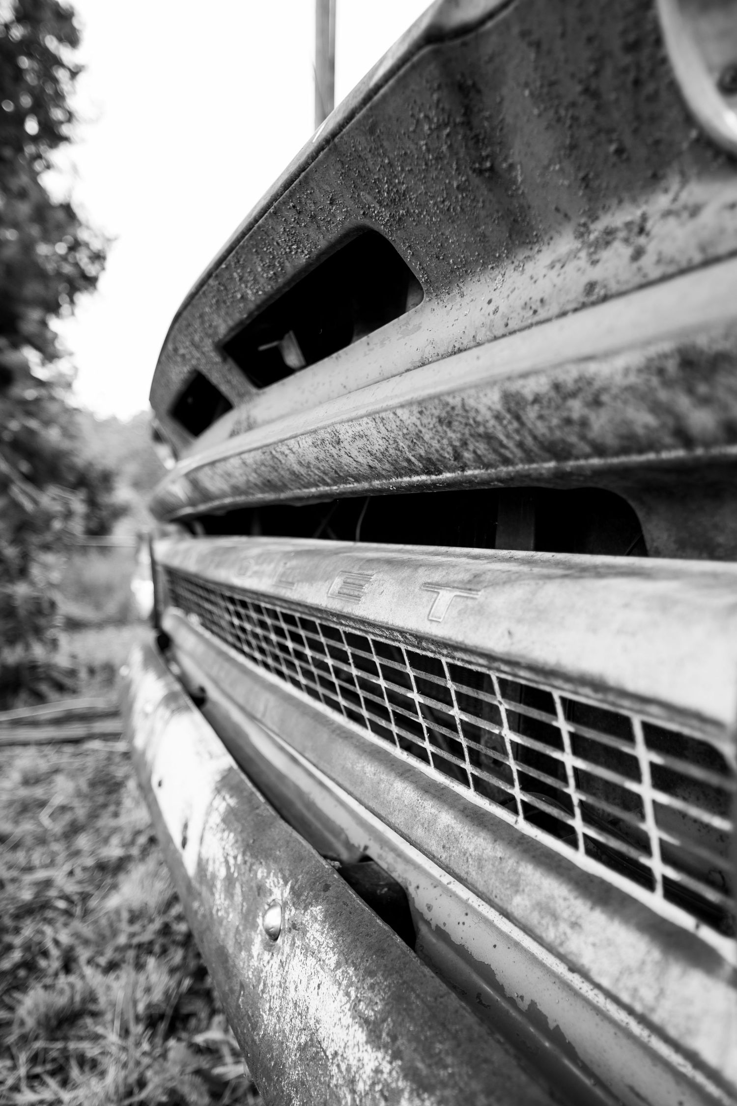 Close-up black and white photograph of a vintage truck grille showing weathered metal and geometric mesh pattern details.