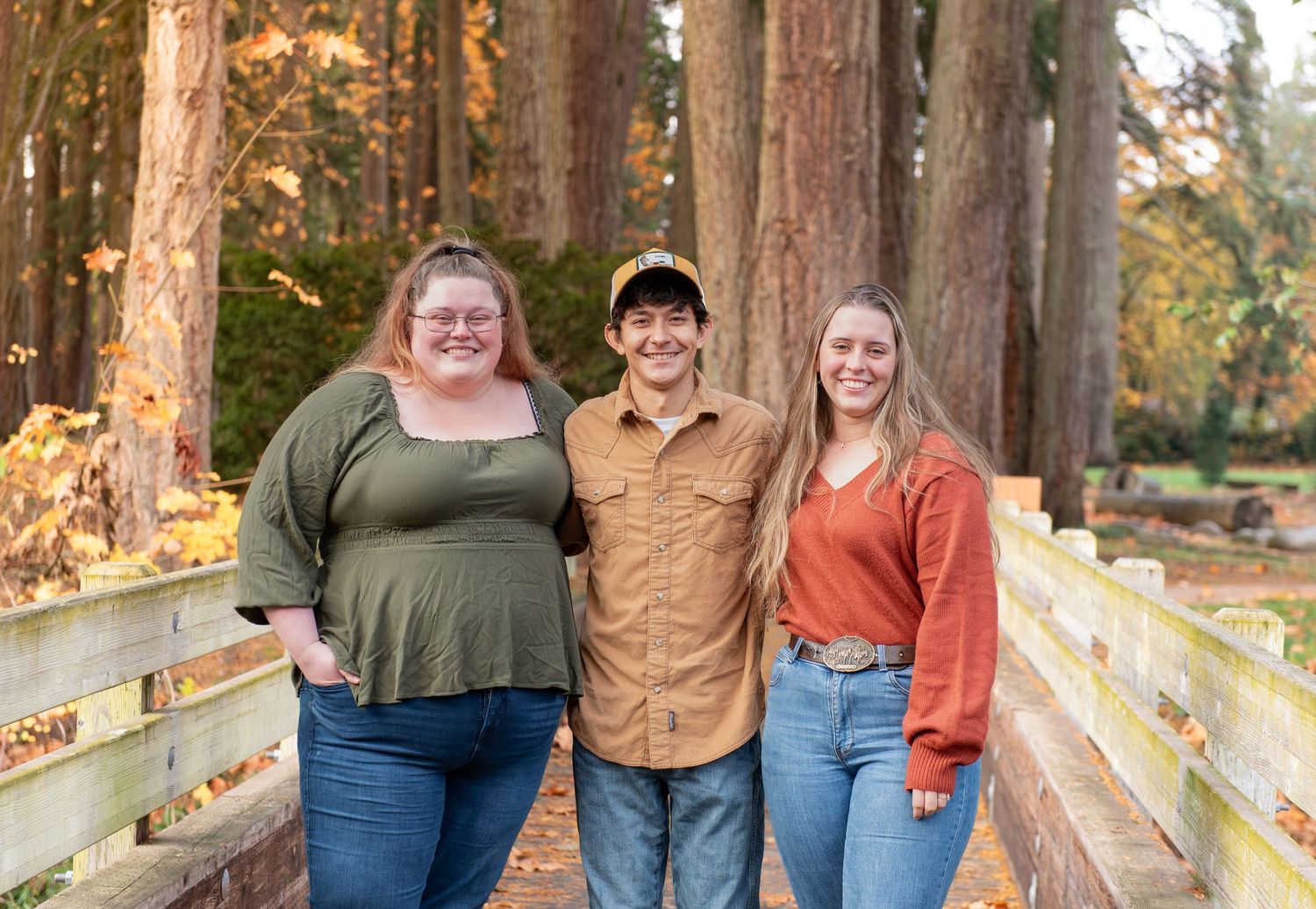 A group of people stand together on a wooden bridge surrounded by tall trees in autumn. located in Stayton, OR