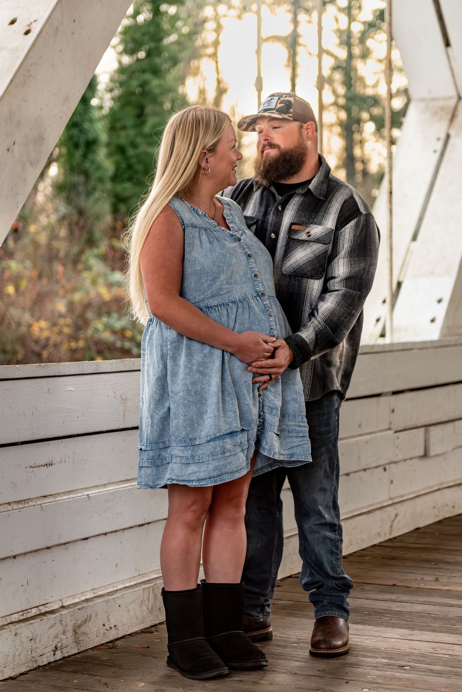 Couple posed looking at each other embracing mama's baby bump for a maternity session located under a covered bridge in Stayton, OR.