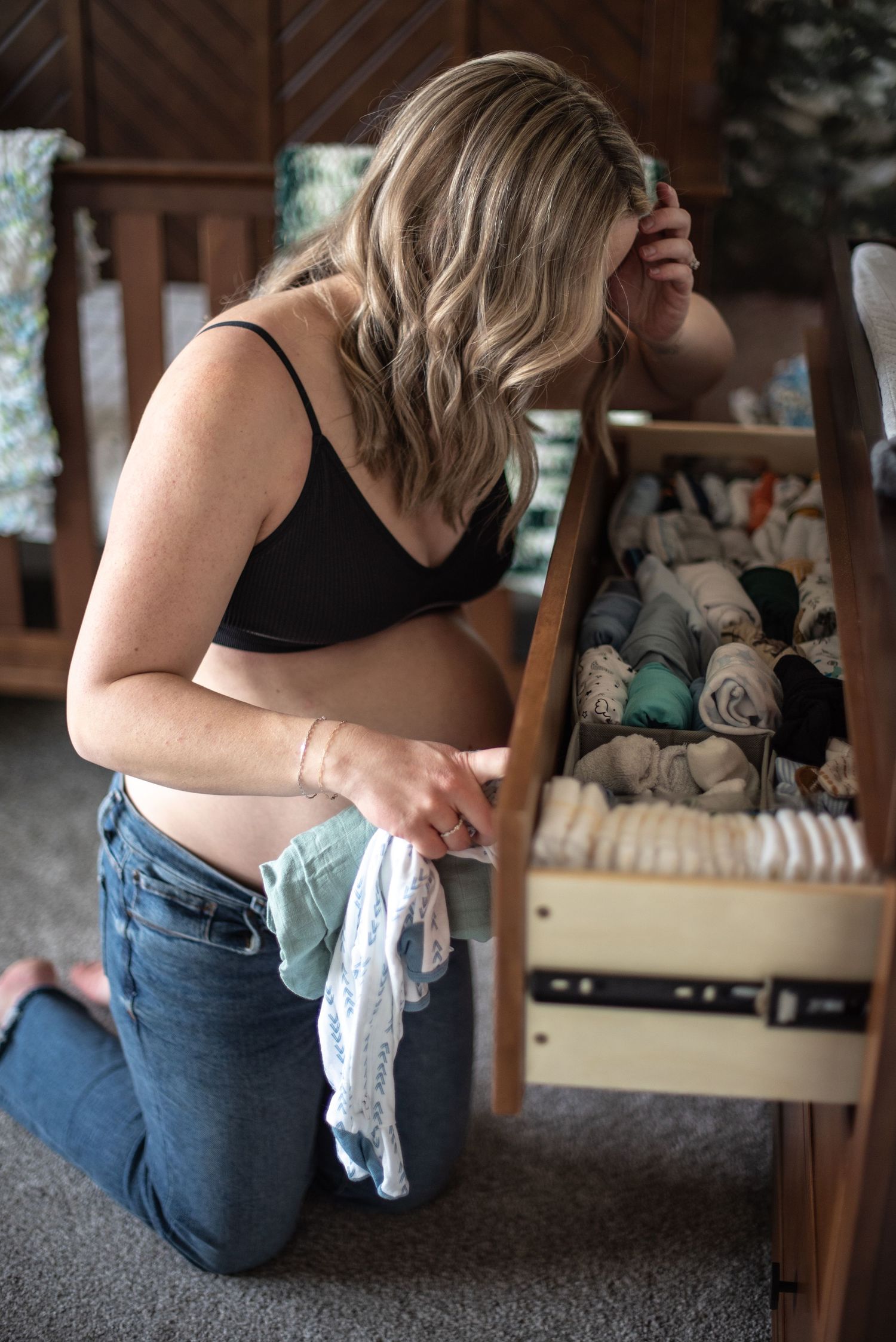 Mom picking a baby outfit in a nursery setting during a maternity photo session in home. Located in Salem, OR