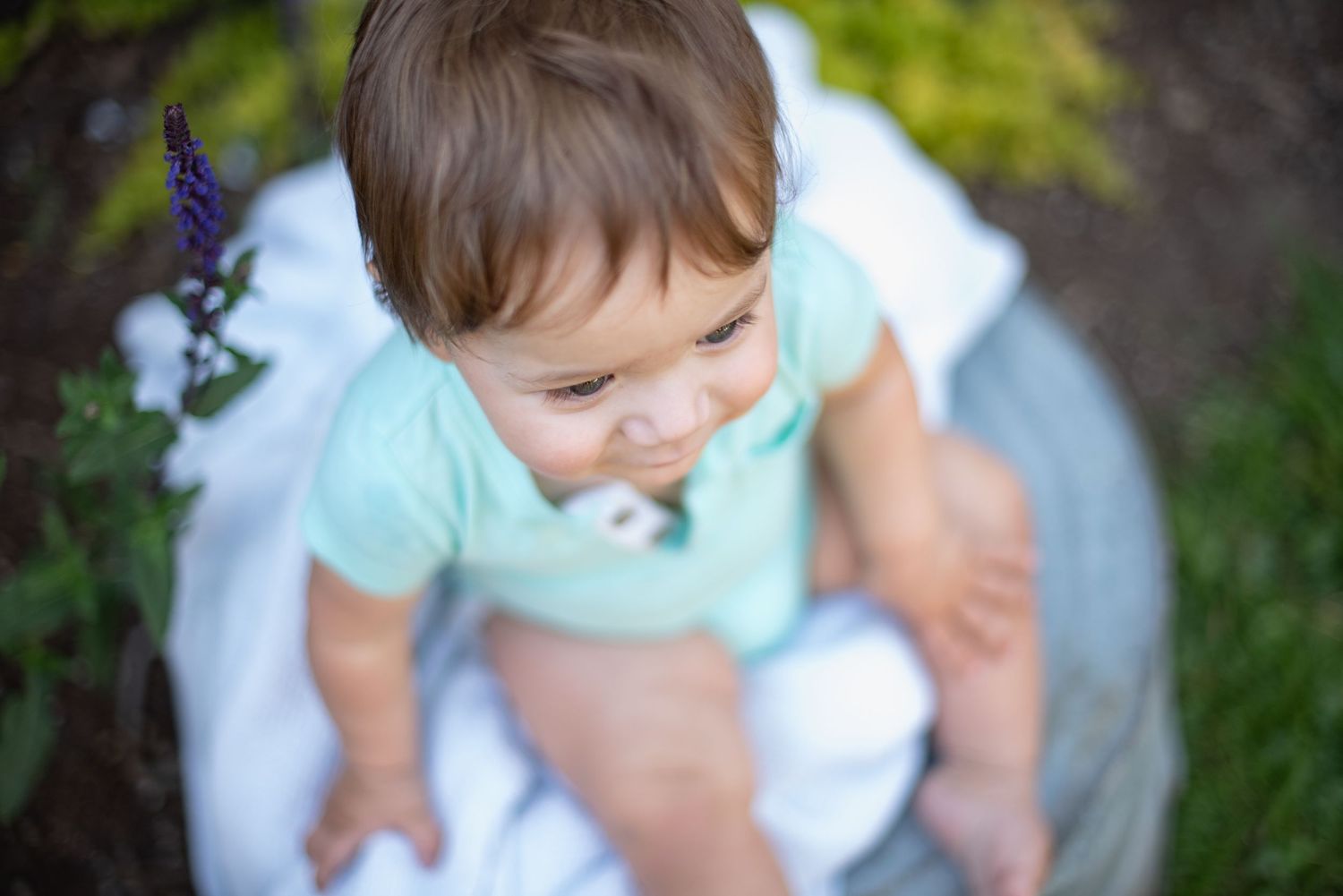 A young child in a light blue shirt explores a garden path surrounded by lush greenery.