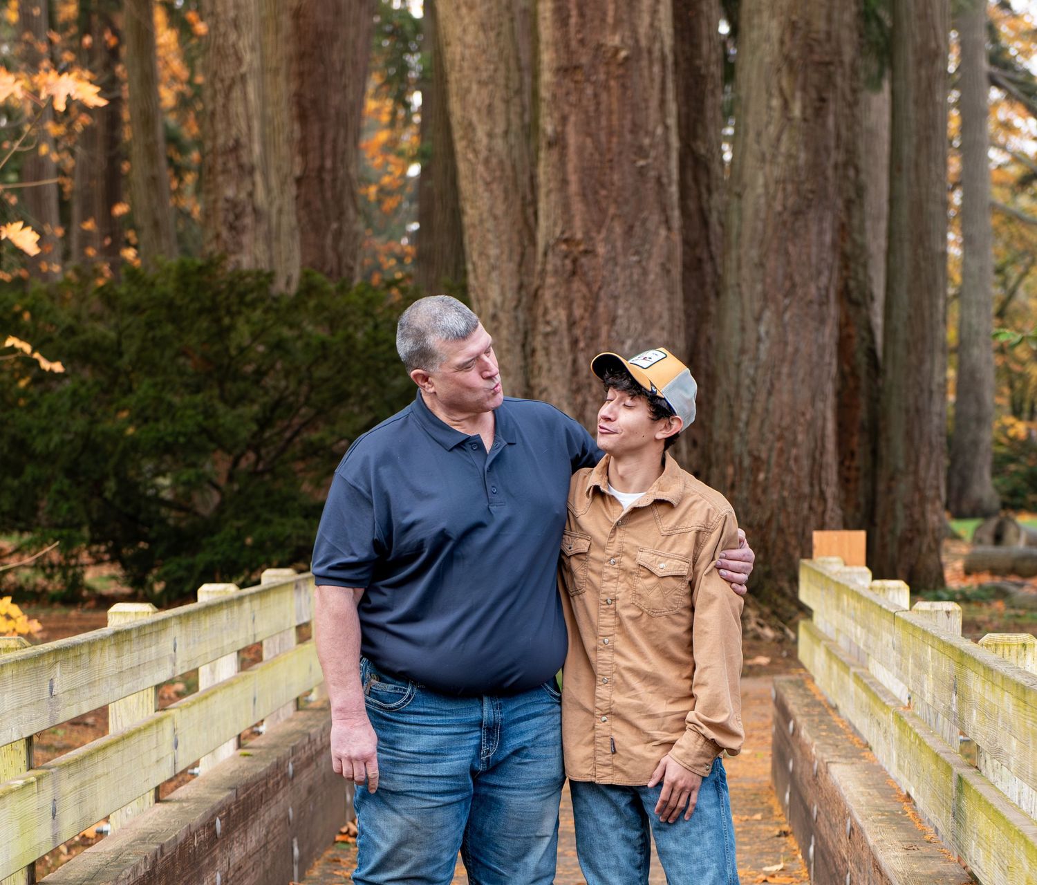 Two people share a happy moment while walking on a wooden bridge covered in autumn leaves through a forest. located in Stayton, OR