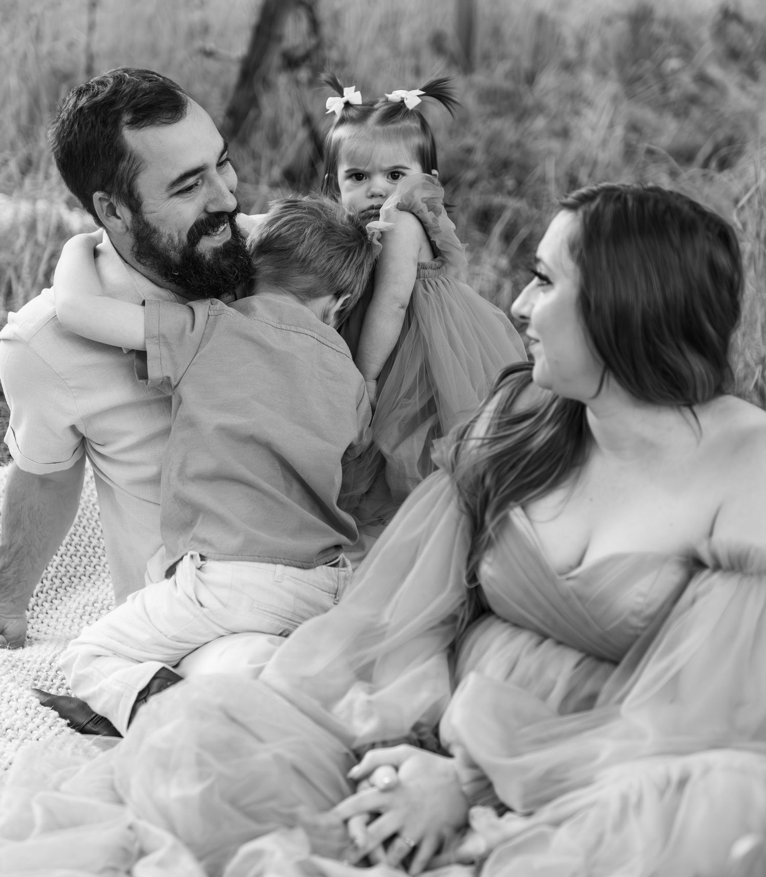Family of four portrait located in a field with fall colored trees in the background and natural golden hour light. Located in Salem, OR