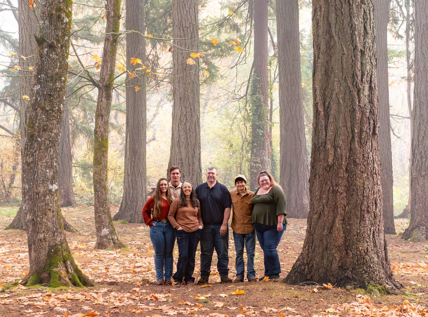 Family Session of parents and adult children gathered in a forest among fir trees on a foggy morning in Stayton, OR.