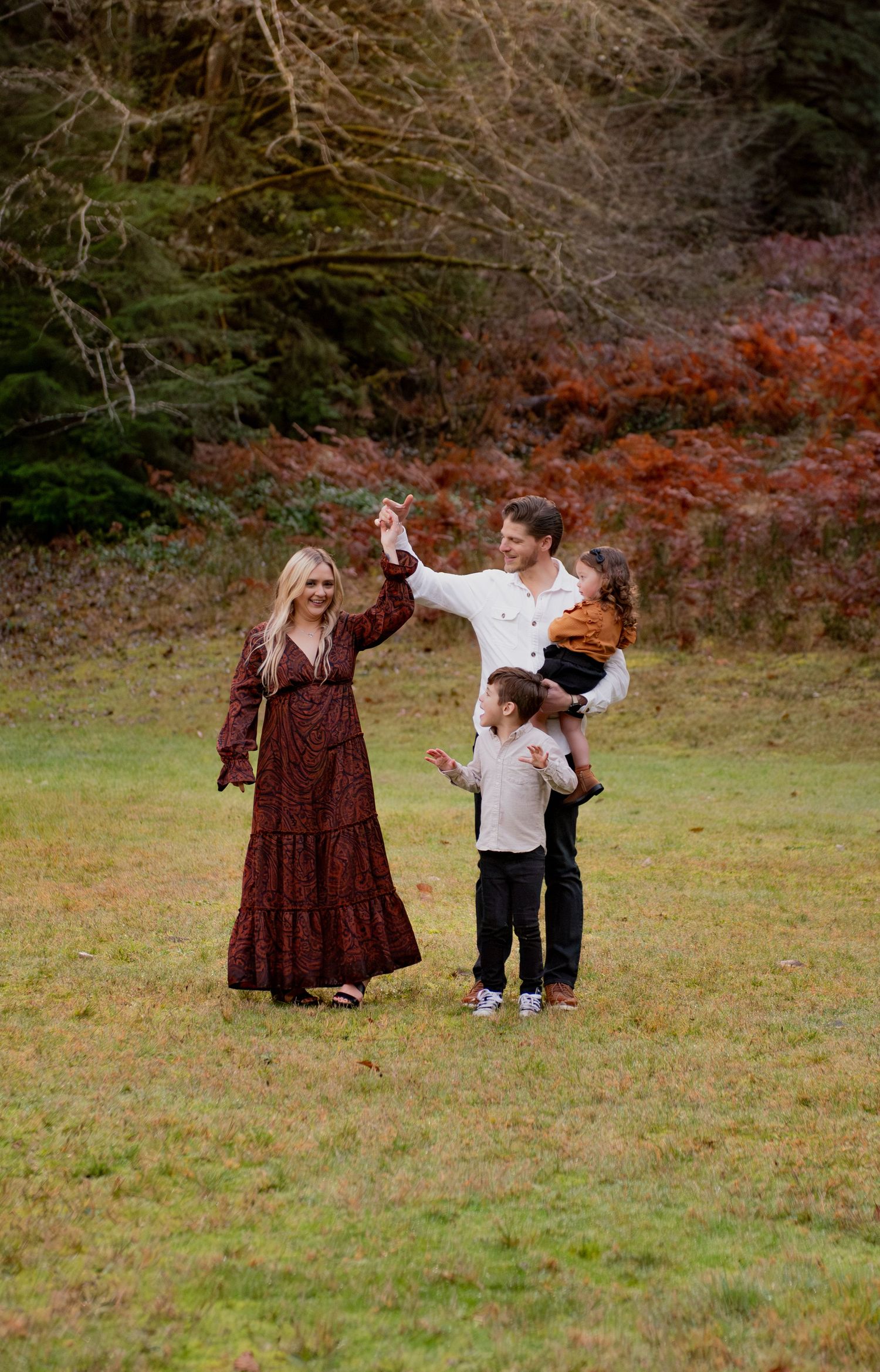A family enjoys a playful moment together in a grassy field with autumn foliage in the background. Silver Falls State Park OR