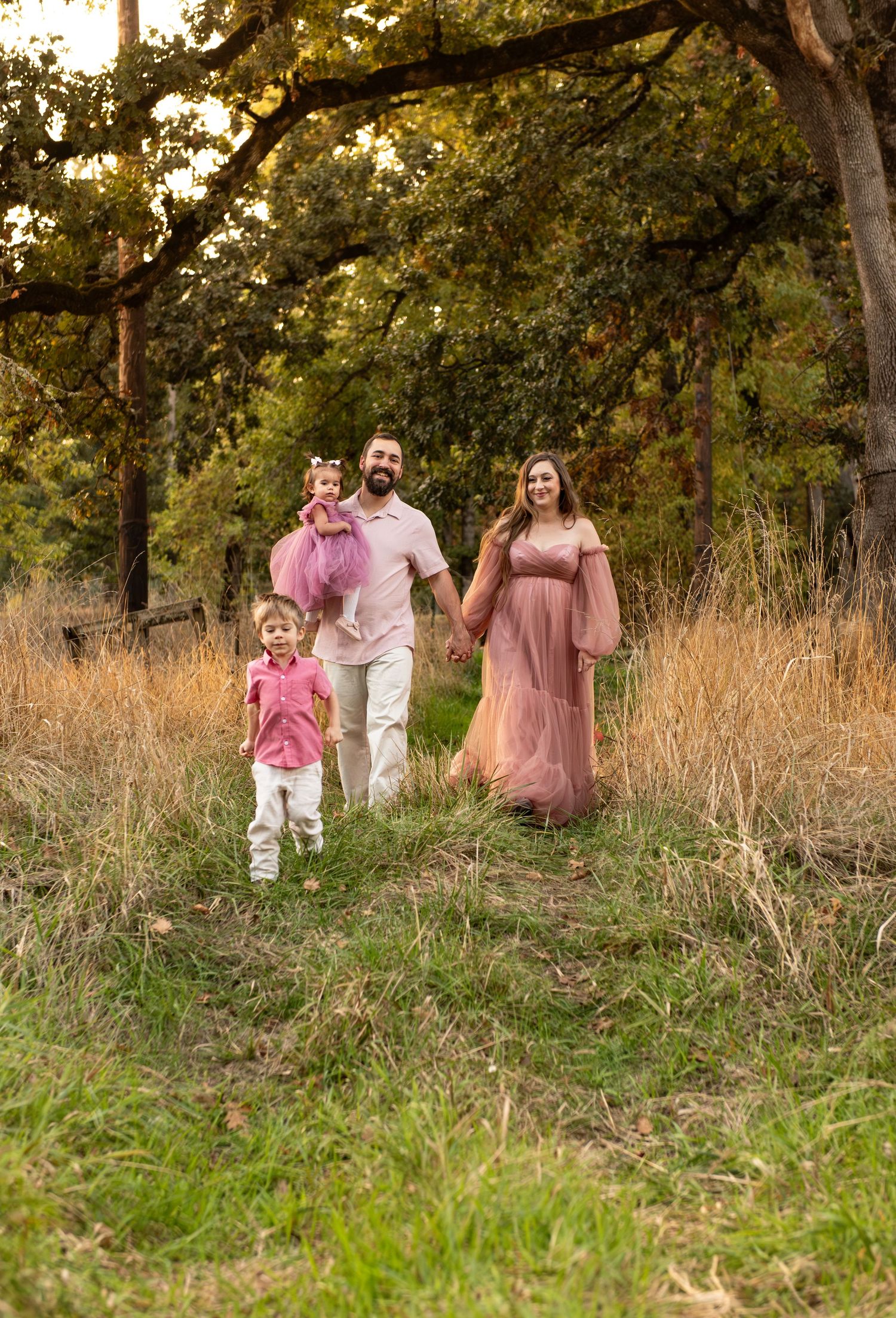 Family of four portrait located in a field with fall colored trees in the background and natural golden hour light. Located in Salem, OR