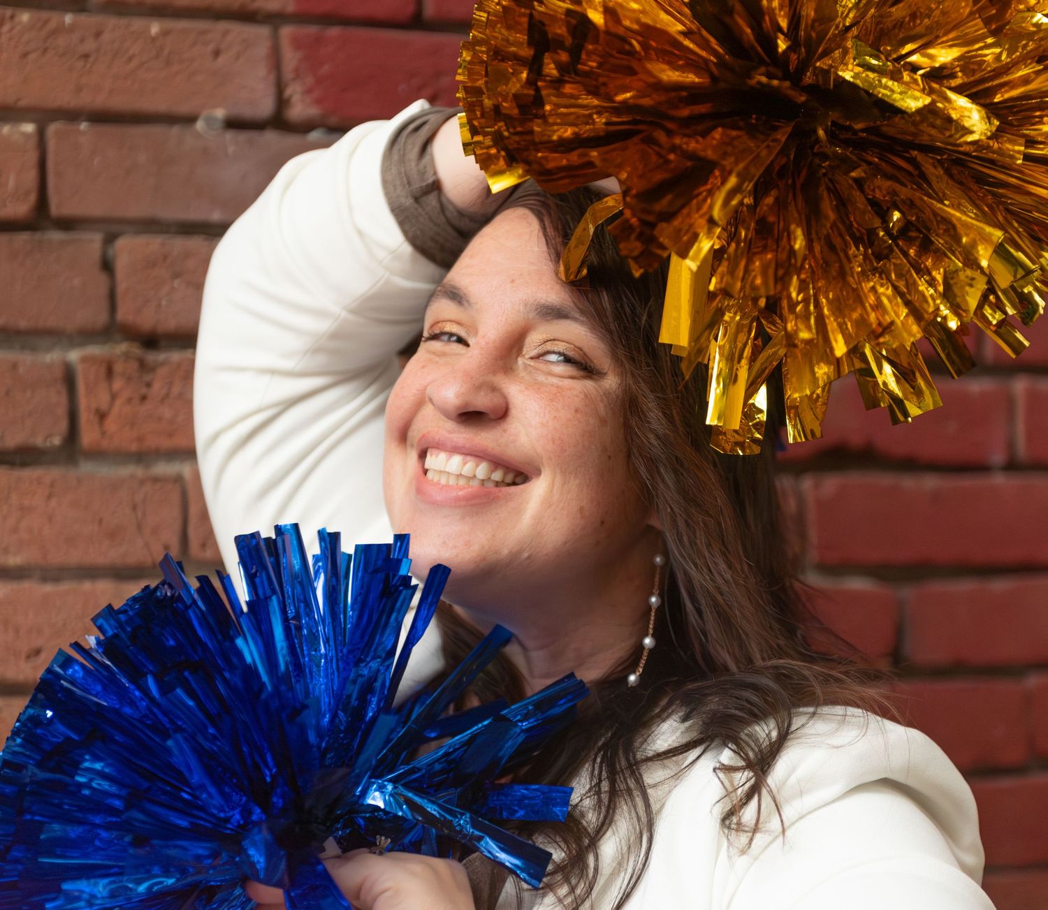 Headshot of woman with pompoms blue and gold with red brick background, for branding images, located in Salem, OR.