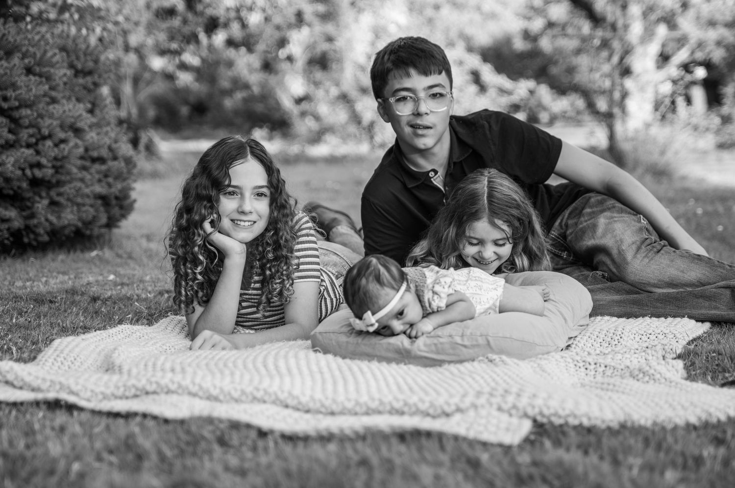 Four children gathered on a blanket in a grassy area in a park, smiles and giggles, Salem, OR.