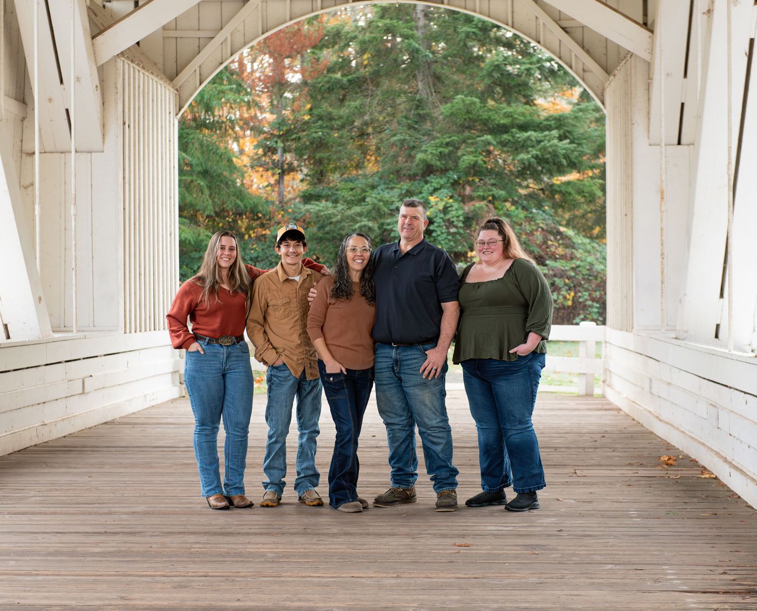 A group of people stand together on a wooden covered bridge surrounded by tall trees in autumn. located in Stayton, OR