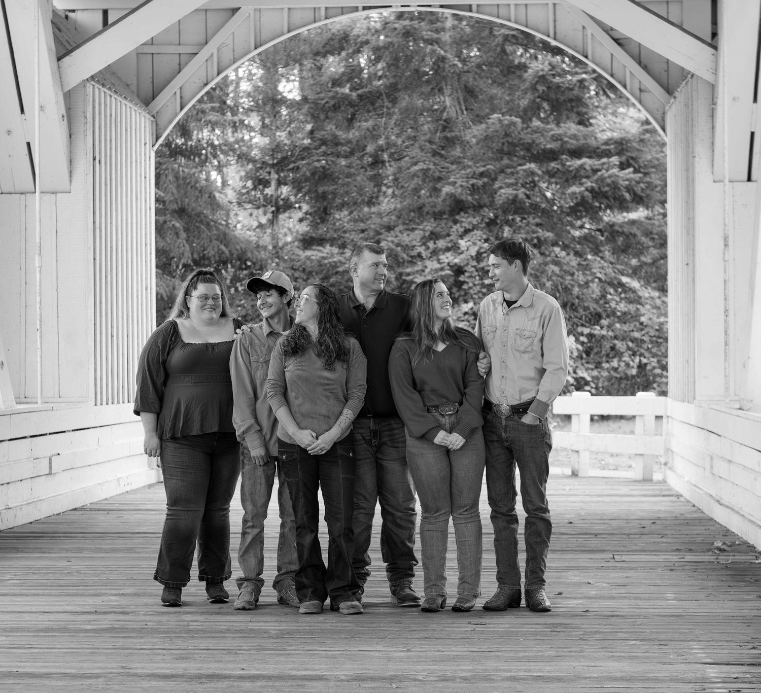 A group of people stand together on a wooden covered bridge surrounded by tall trees in autumn. located in Stayton, OR