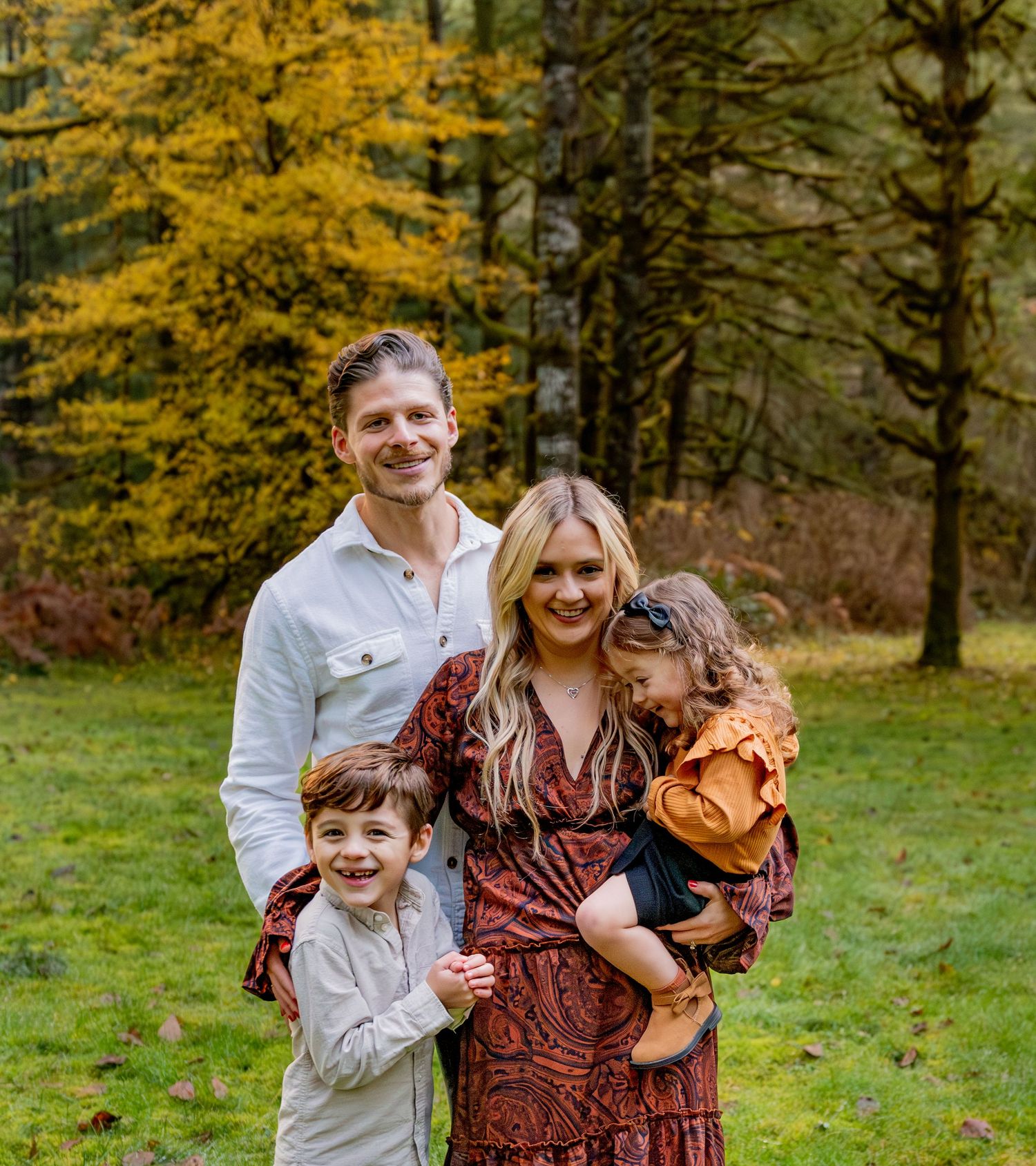 Rich fall colors family posed together in a grassy area with fall foliage in the background.  everyone smiling and laughing Silver Falls, OR
