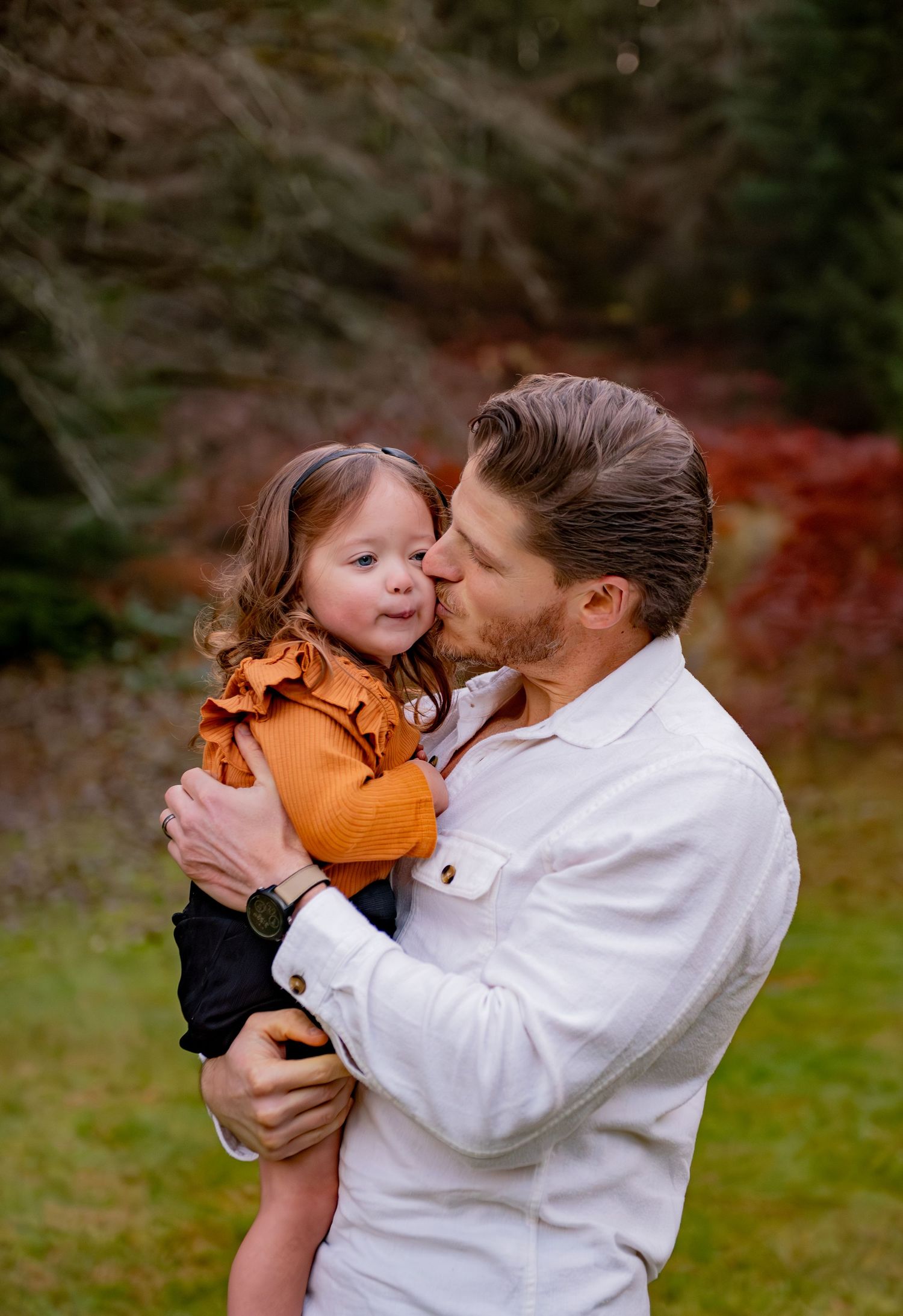A parent in a white shirt shares tender moments of affection with a small child wearing orange outdoors. Silver Falls State Park OR