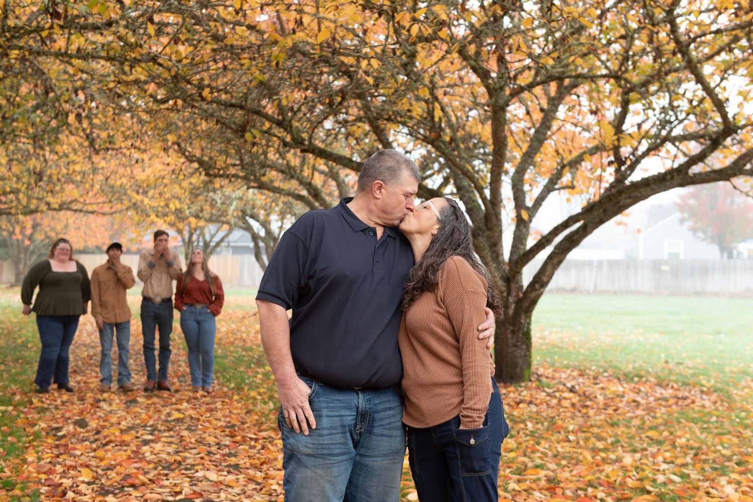 Group poses together under autumn trees with golden leaves and fallen foliage on the ground during a fall photo session. Stayton, OR