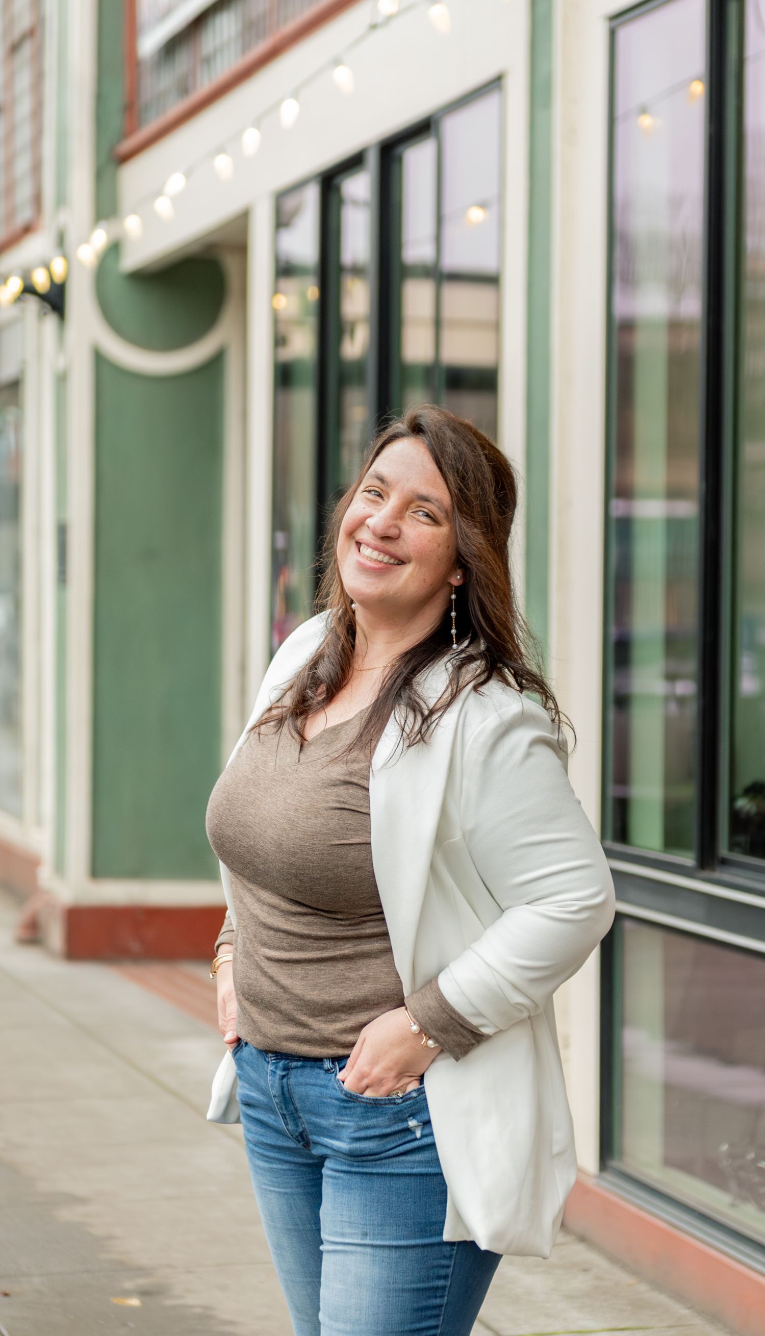 Author posed on a sidewalk with a beautiful storefront and string lights in the background. Downtown Salem, OR