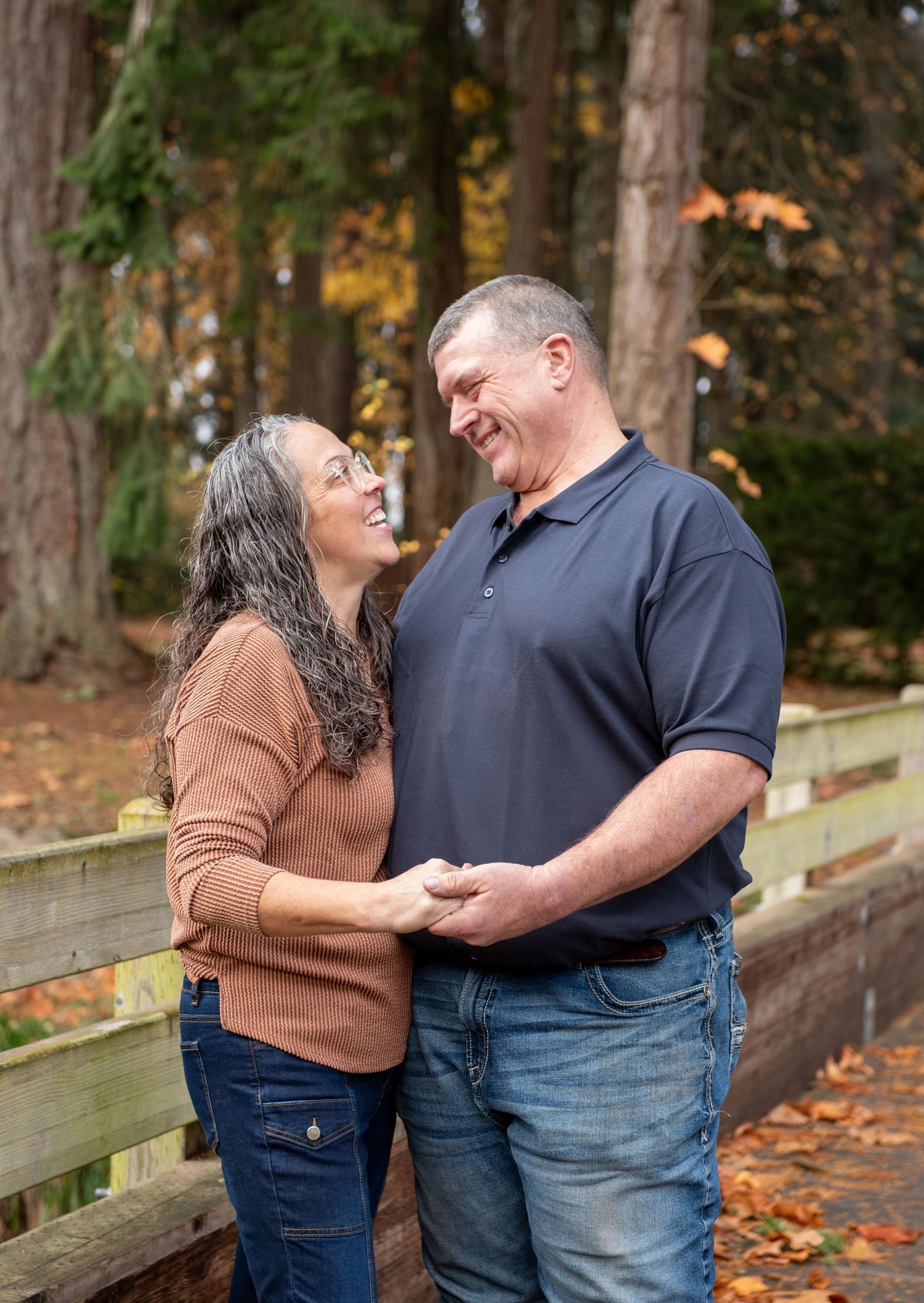 A couple shares joyful laughter while leaning against a wooden bridge surrounded by autumn leaves in a park setting. located in Stayton, OR