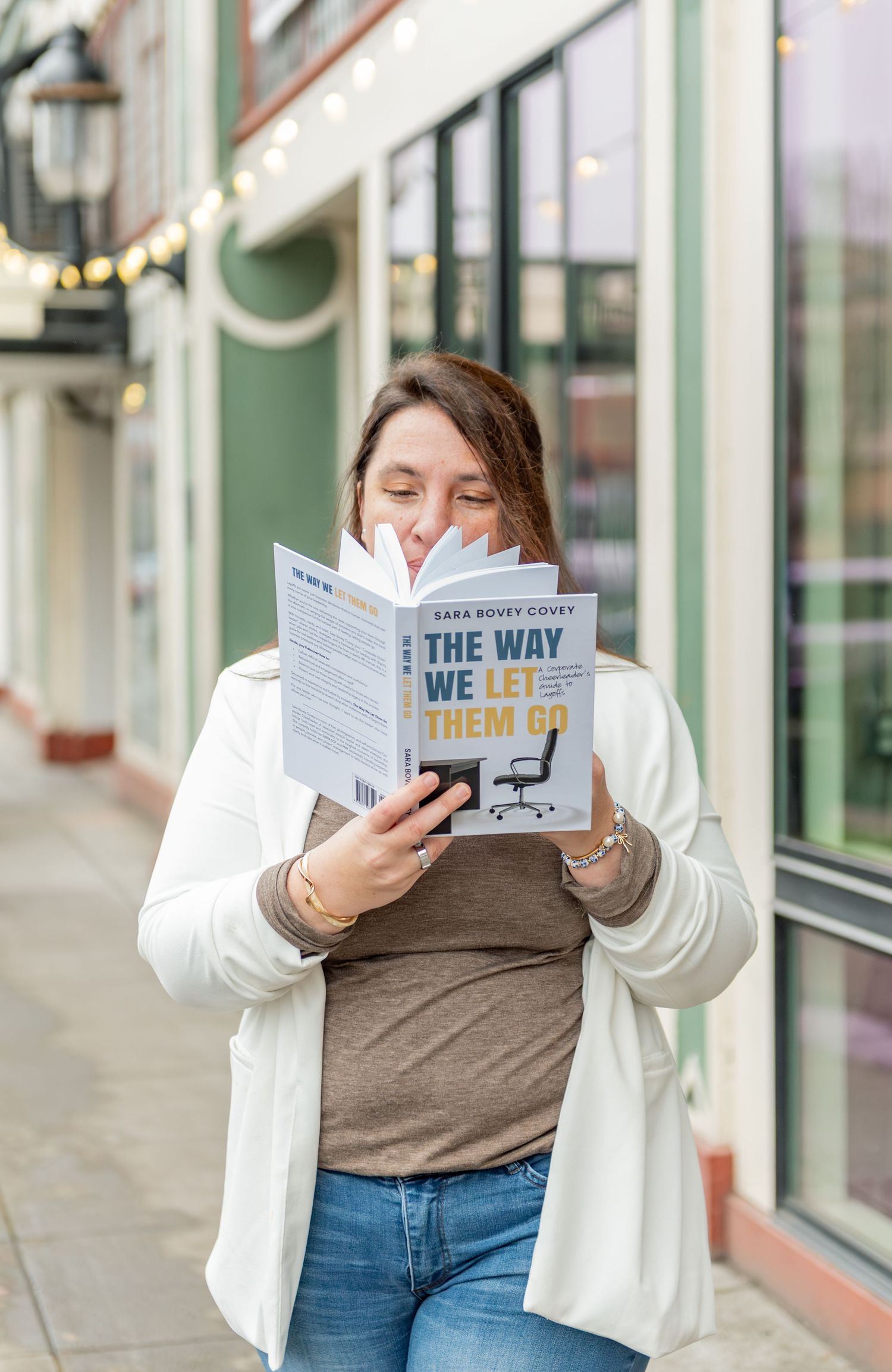 Author reading her book while posed on a sidewalk with a beautiful storefront and string lights in the background. Downtown Salem, OR.