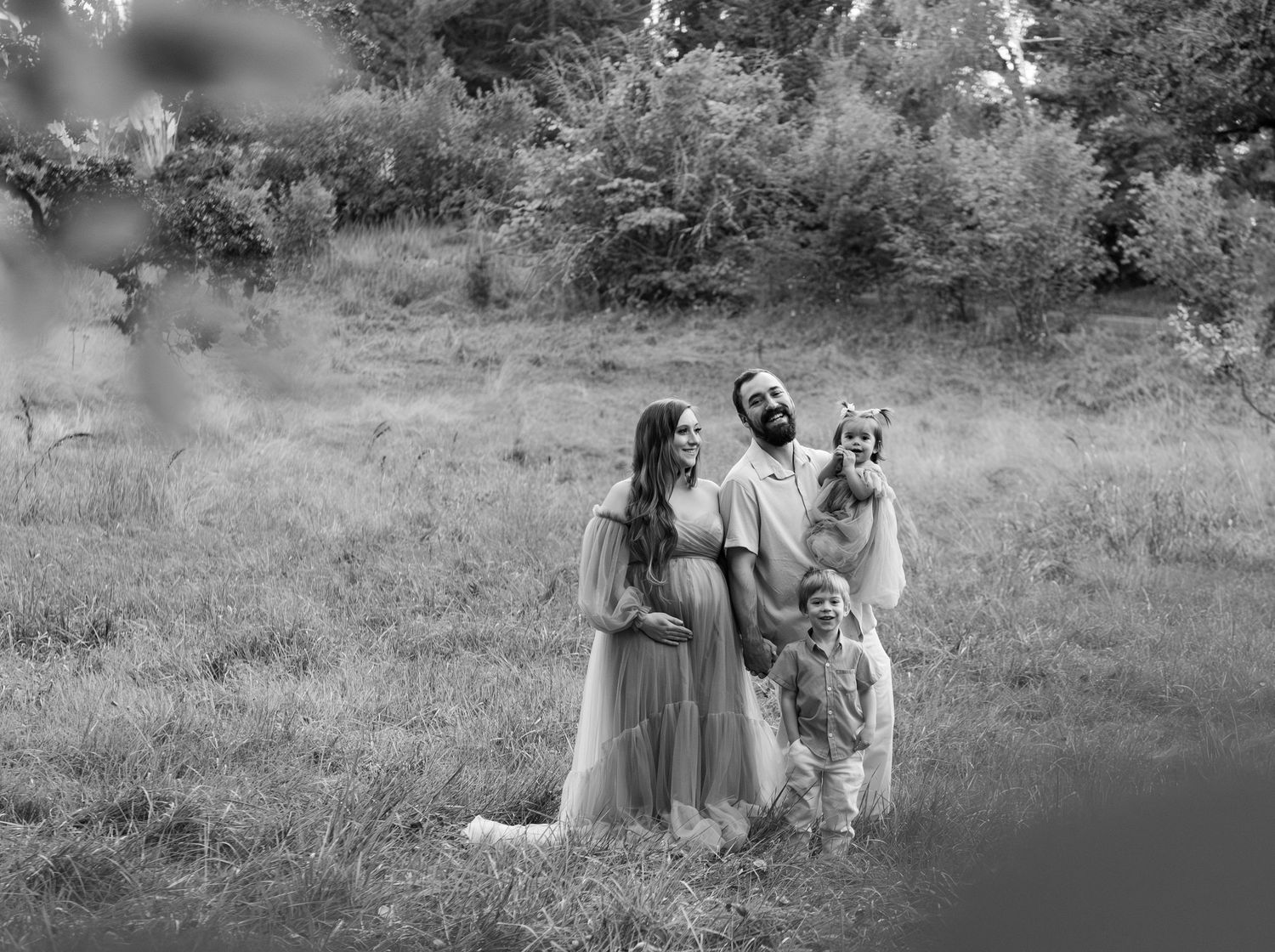 Family of four portrait located in a field with fall colored trees in the background and natural golden hour light. Located in Salem, OR